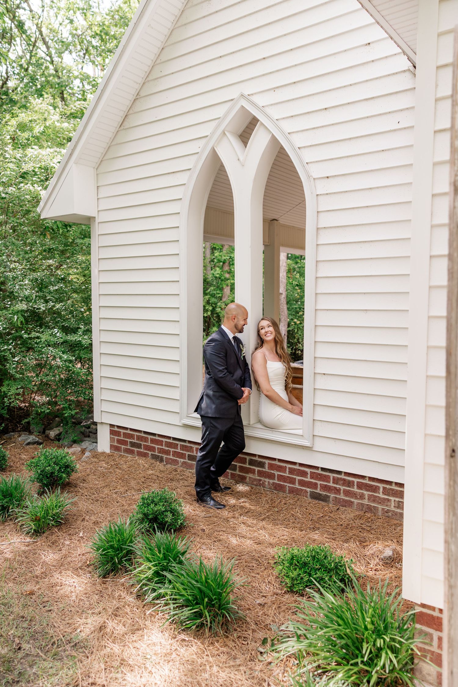 White chapel exterior with arched doorways and landscaped garden during wedding.