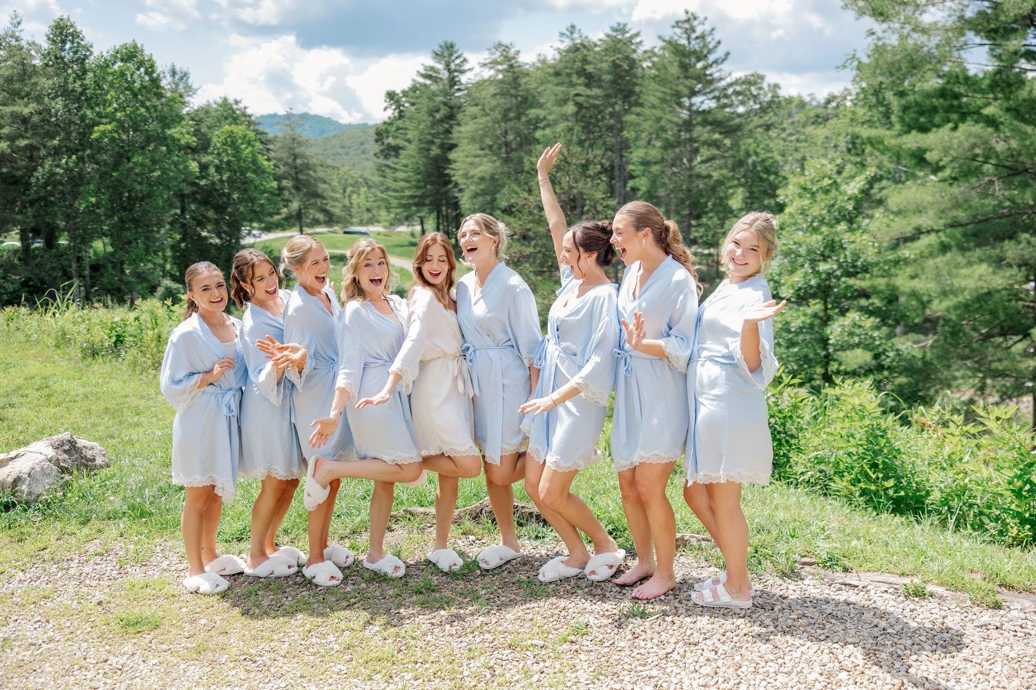 A group in light blue dresses poses together on a sunny mountainside path.