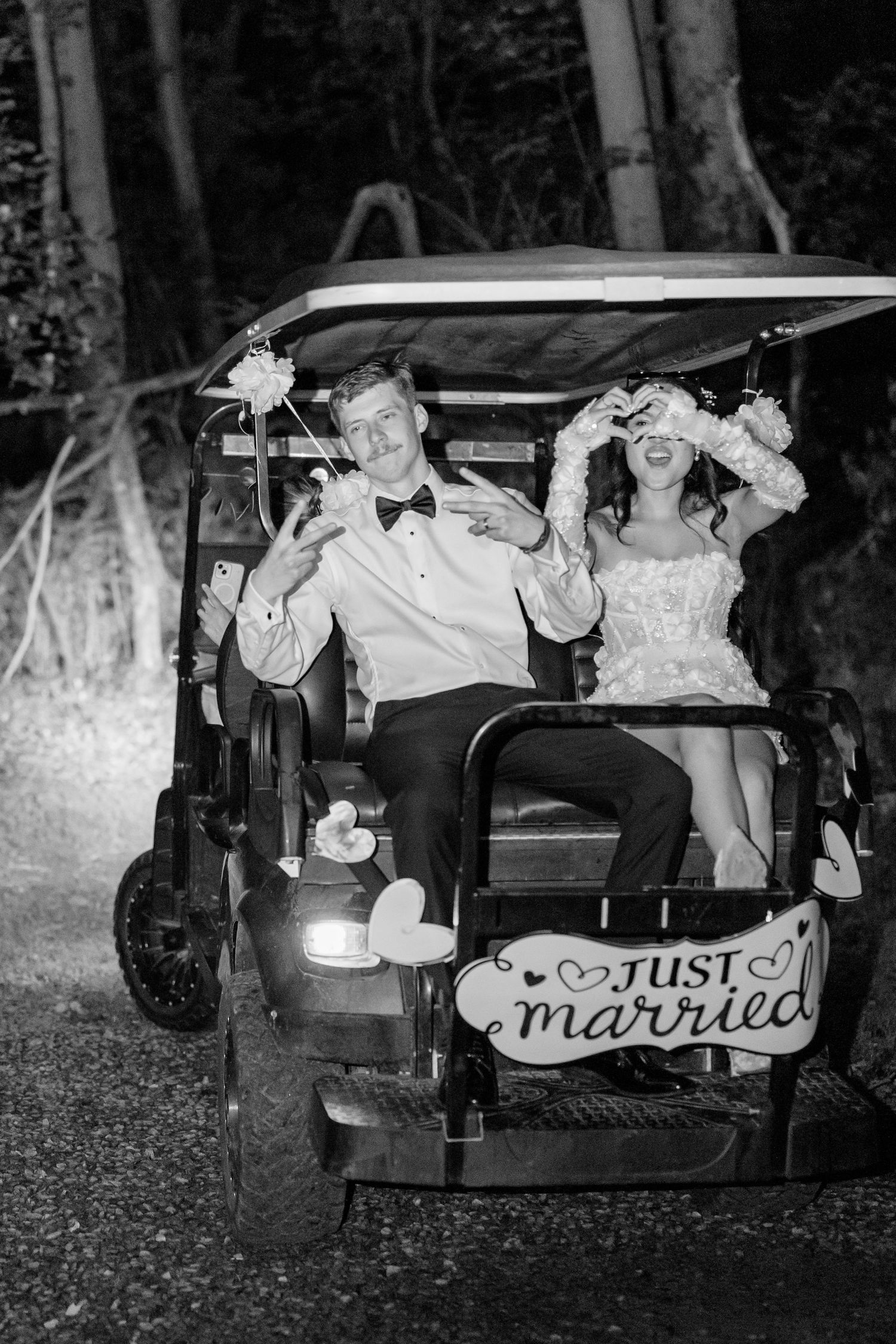 Just married couple poses in vintage golf cart decorated with wedding signage at night.