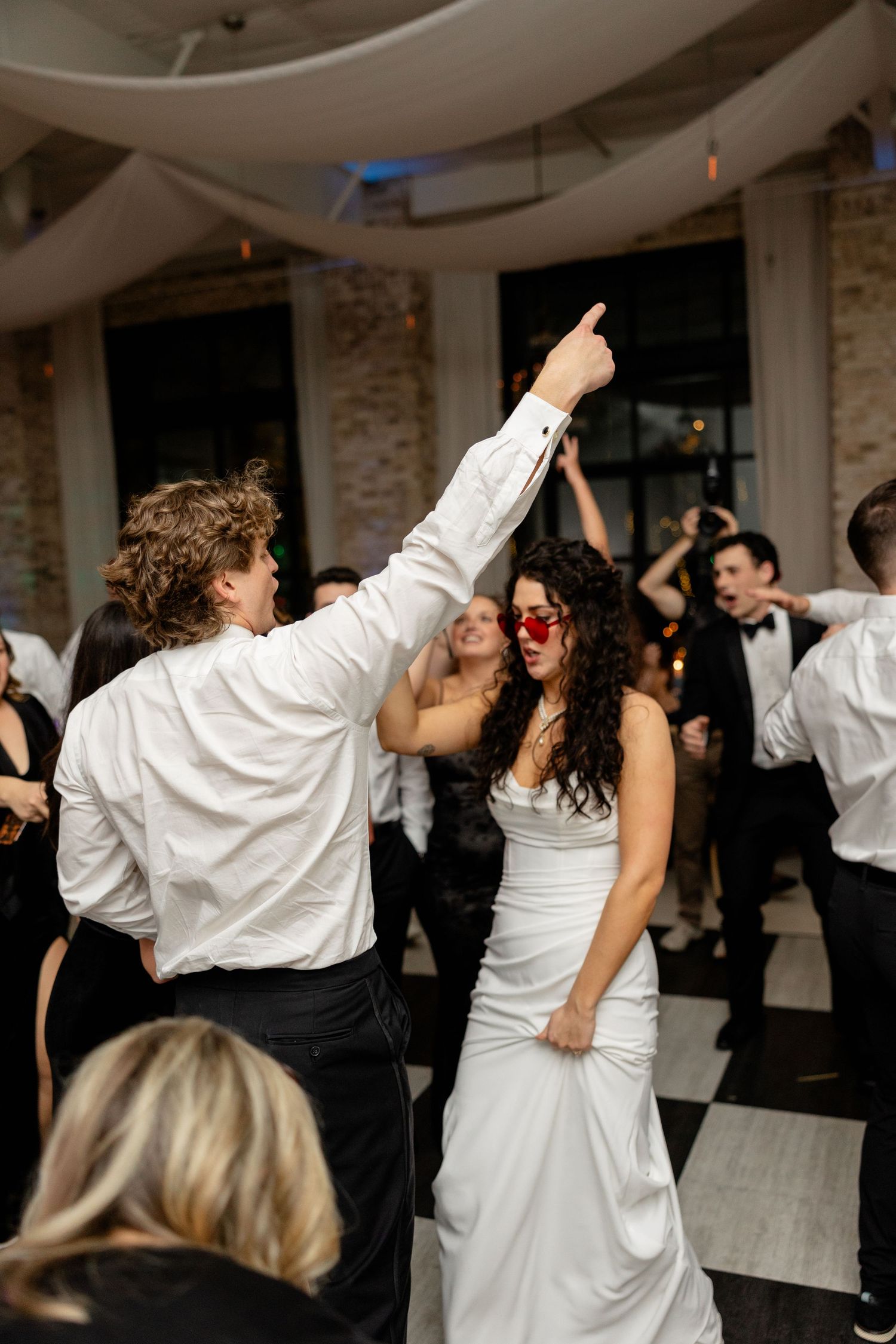 Energetic wedding reception dancing on a black and white checkered floor.