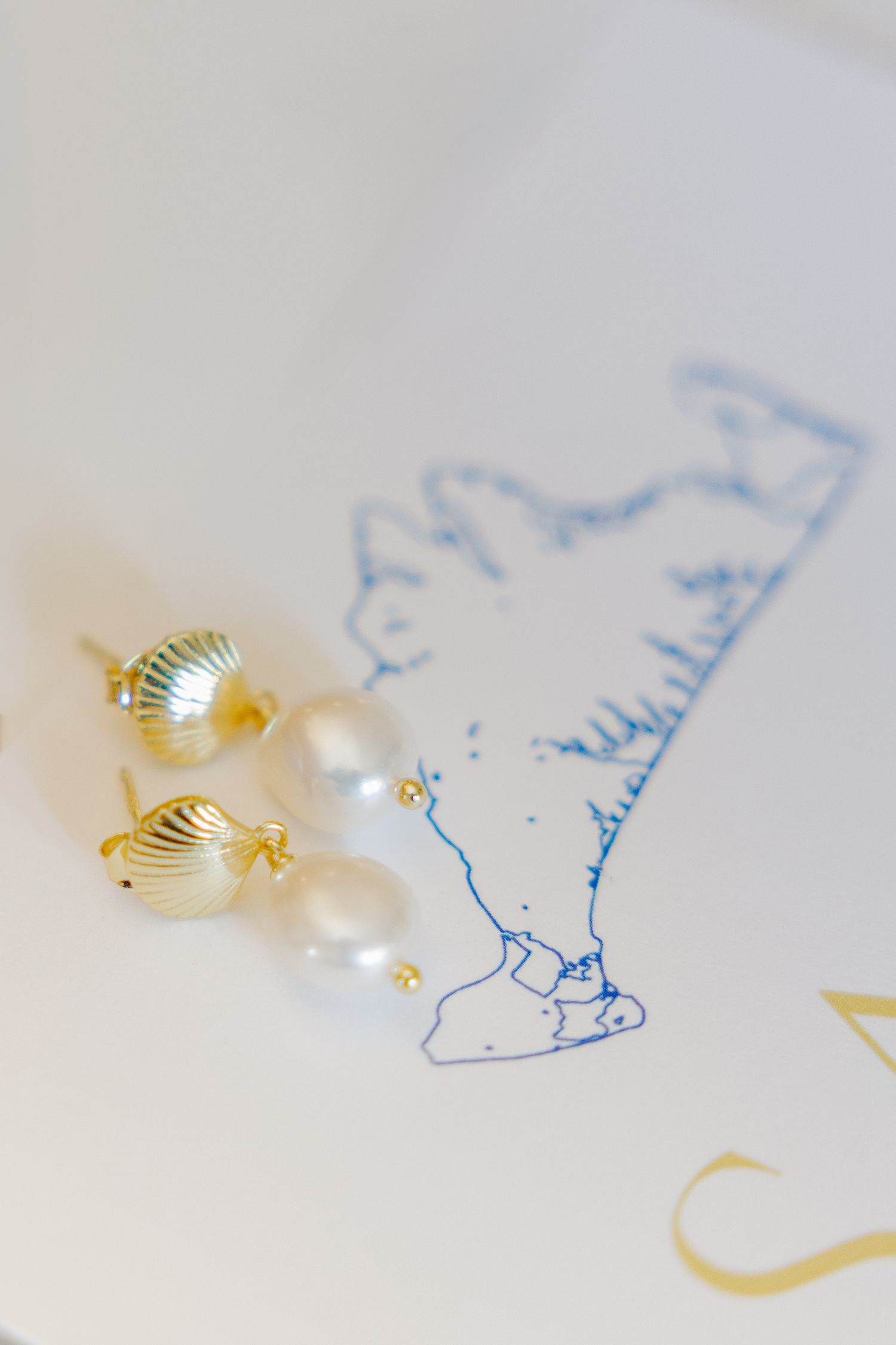 Gold and pearl drop earrings resting on white stationery with blue map illustration.
