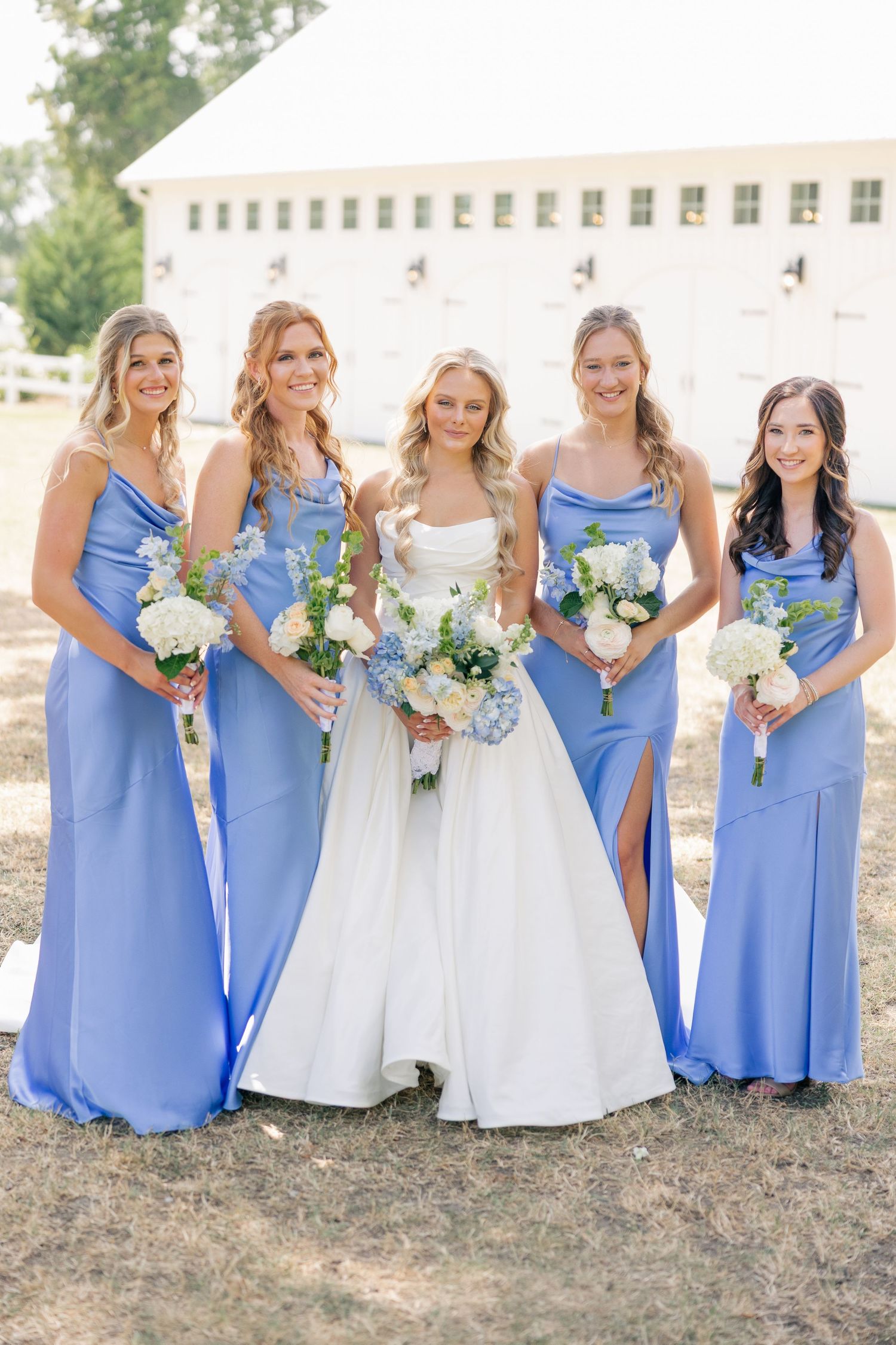 Bride in white gown with four bridesmaids in periwinkle blue dresses holding white bouquets.