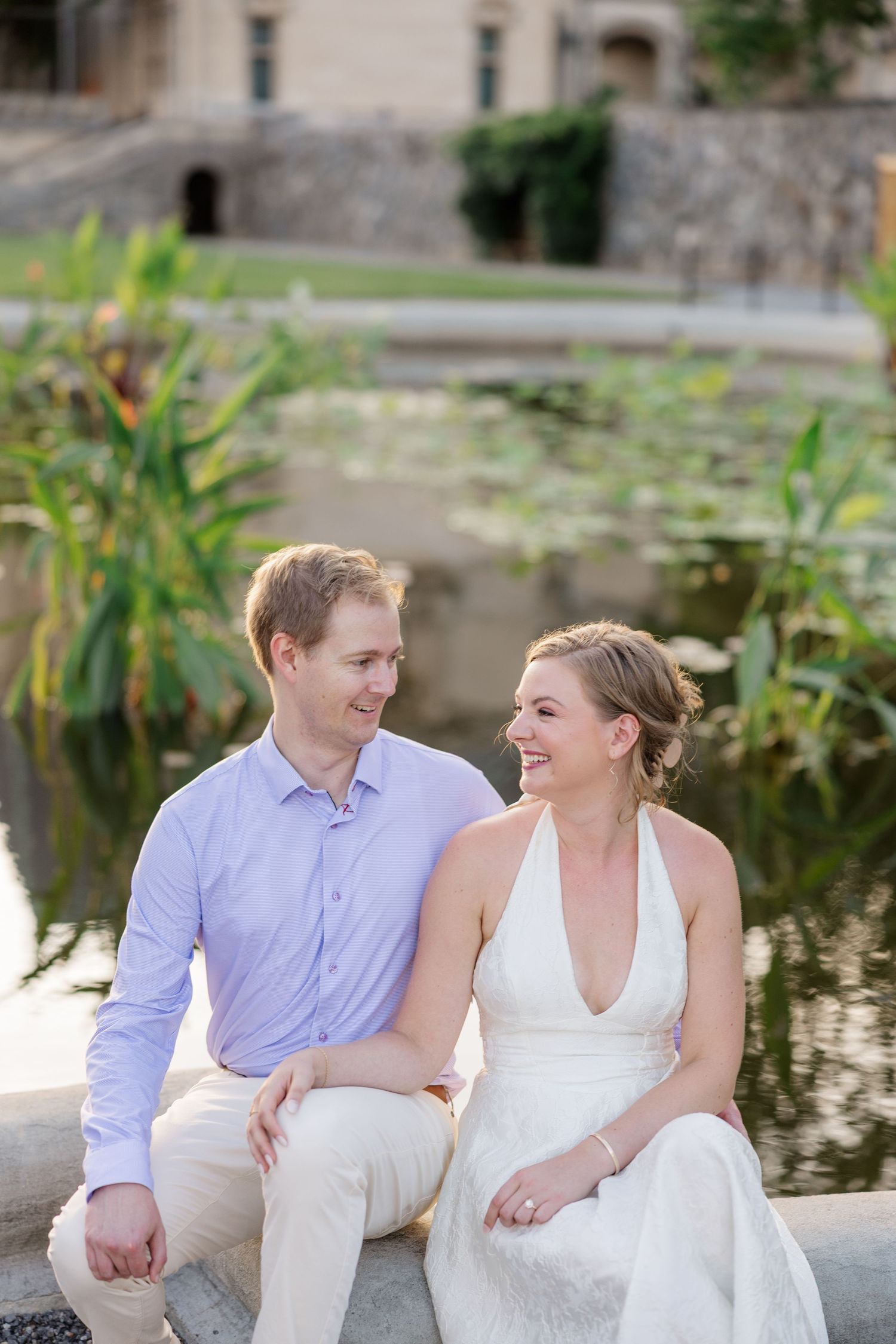A couple sits by a pond sharing a tender moment during an outdoor photo session.