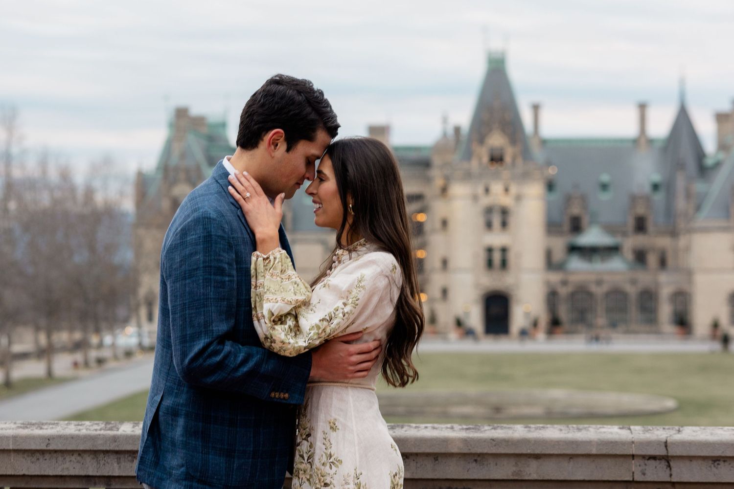 Romantic couple embracing in front of the historic Biltmore Estate in Asheville on a winter afternoon.