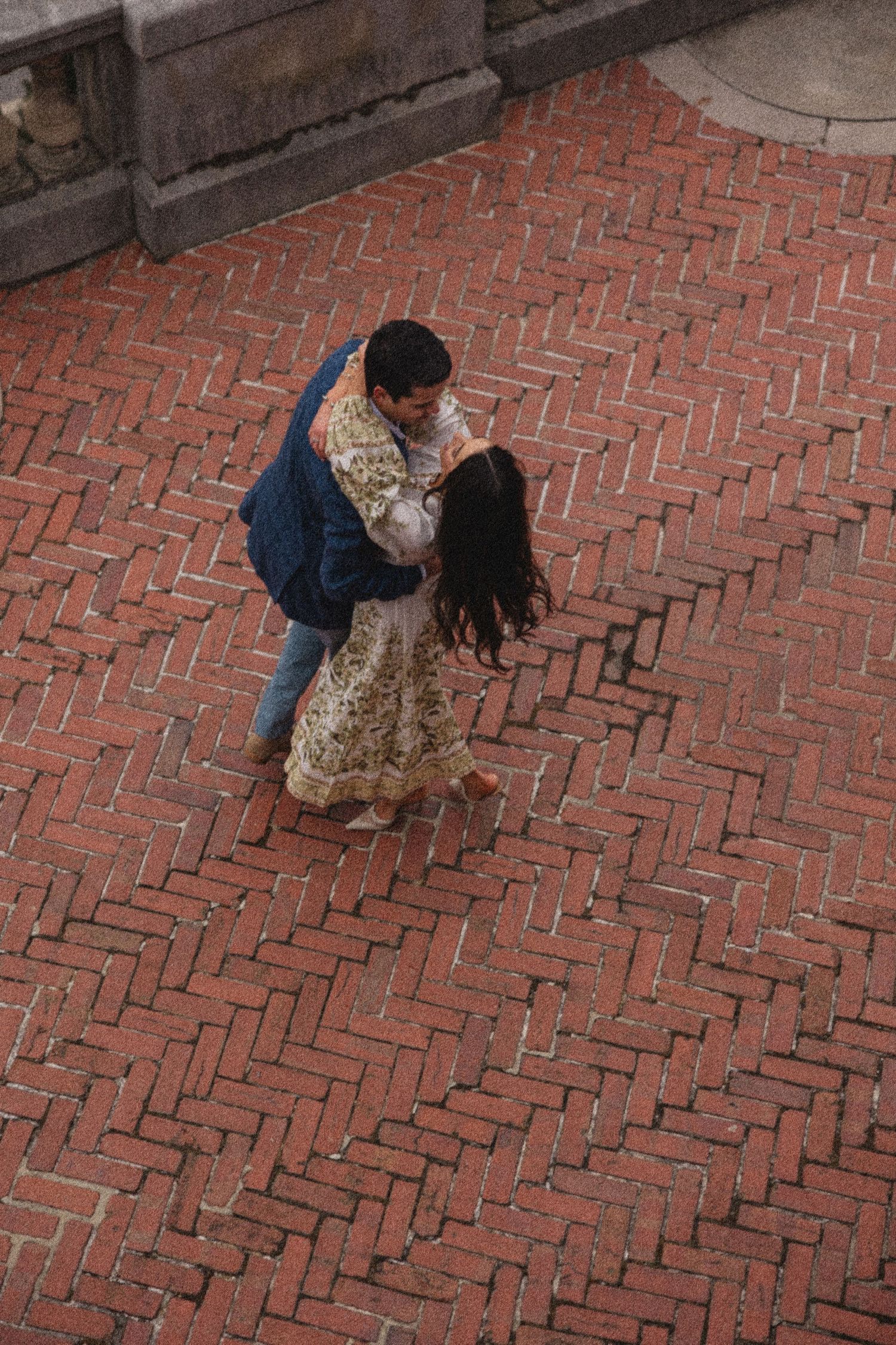 An aerial view shows two people dancing on a herringbone brick patio together in an intimate moment.