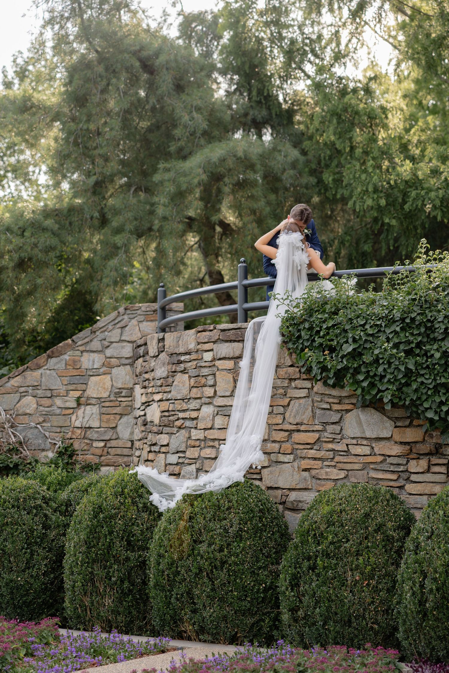 A bride's dress and veil flow dramatically against a stone wall in an outdoor portrait sequence.