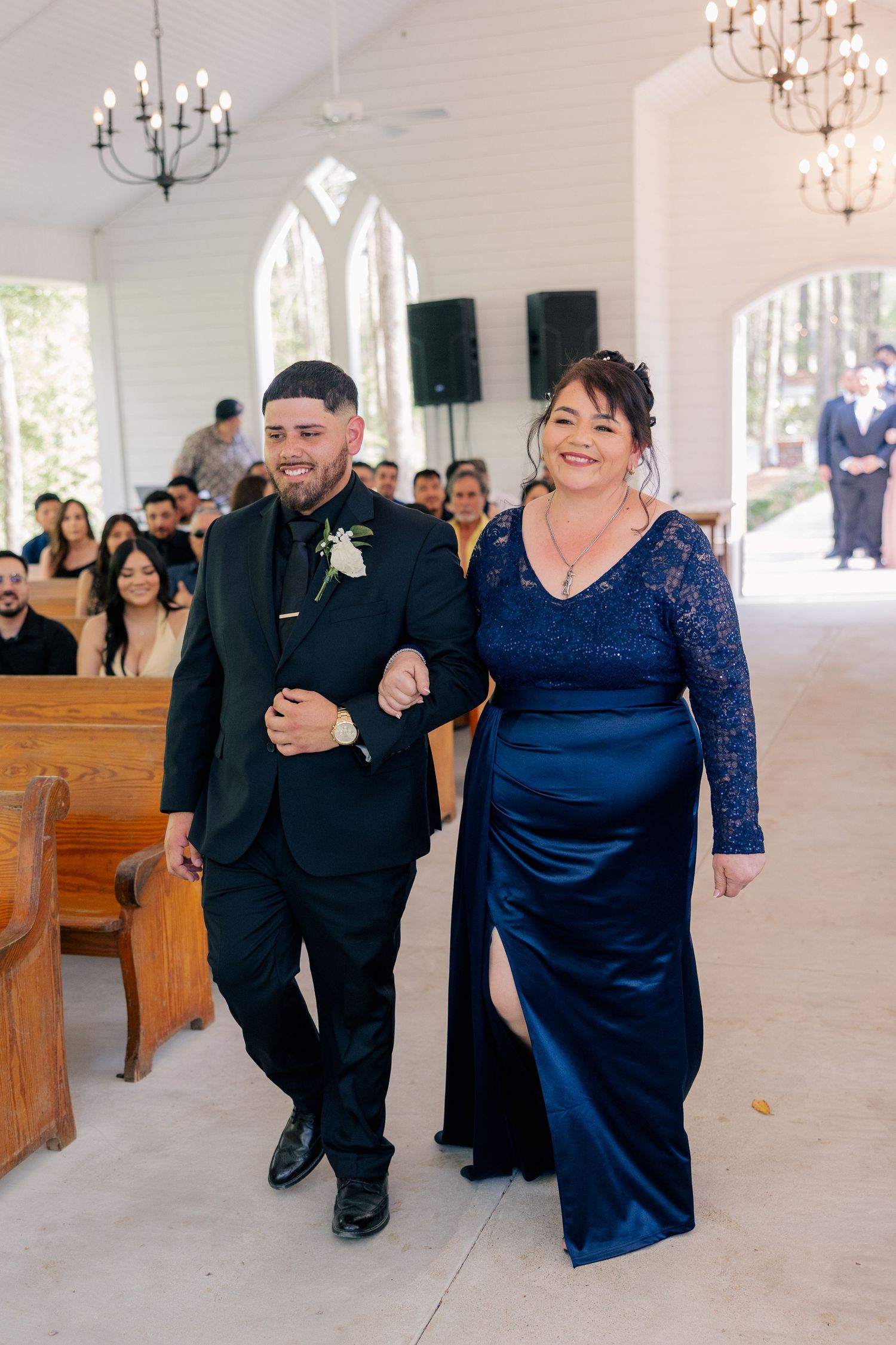 Wedding guests celebrate joyfully while walking down the aisle of a white chapel.