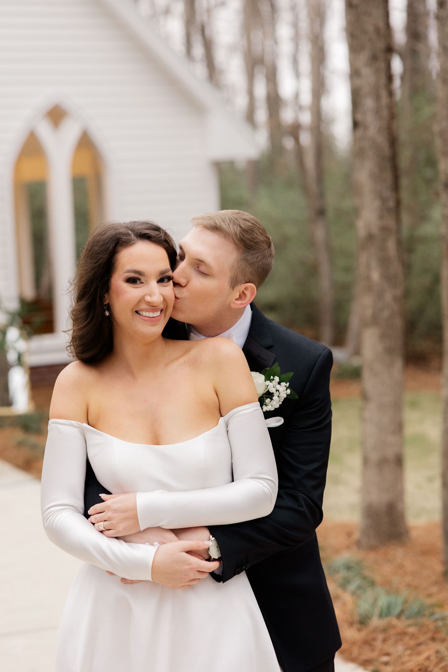 A tender moment between newlyweds shared outside a white chapel on their wedding day.