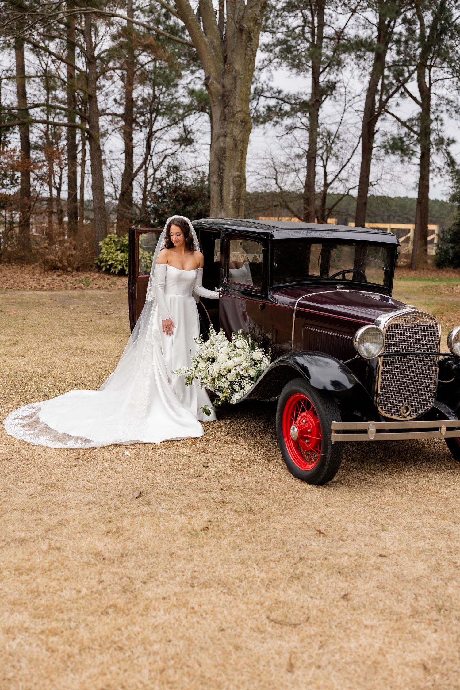 A bridal photo shoot with a classic vintage car against a backdrop of tall pine trees.
