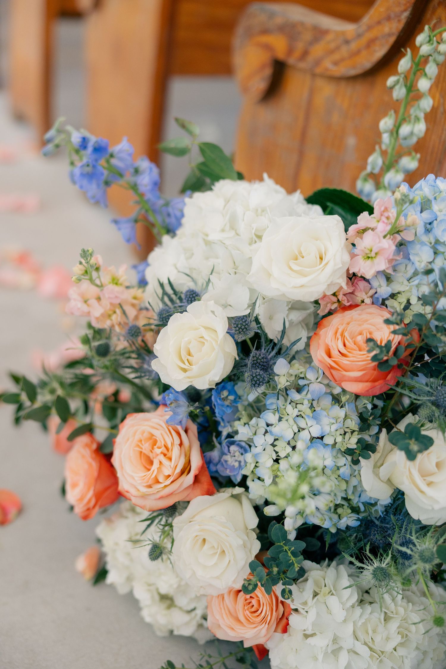 Close-up of romantic wedding bouquet with peach roses, white flowers, and blue delphinium.