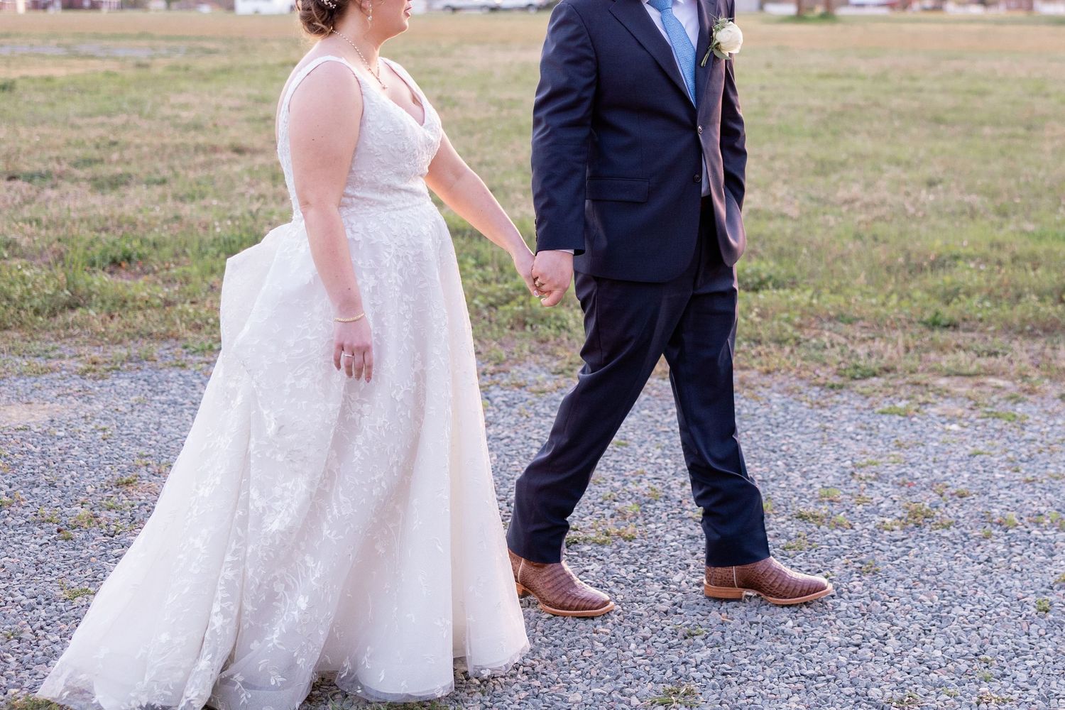 Couple walking together on a gravel path in formal wedding attire.