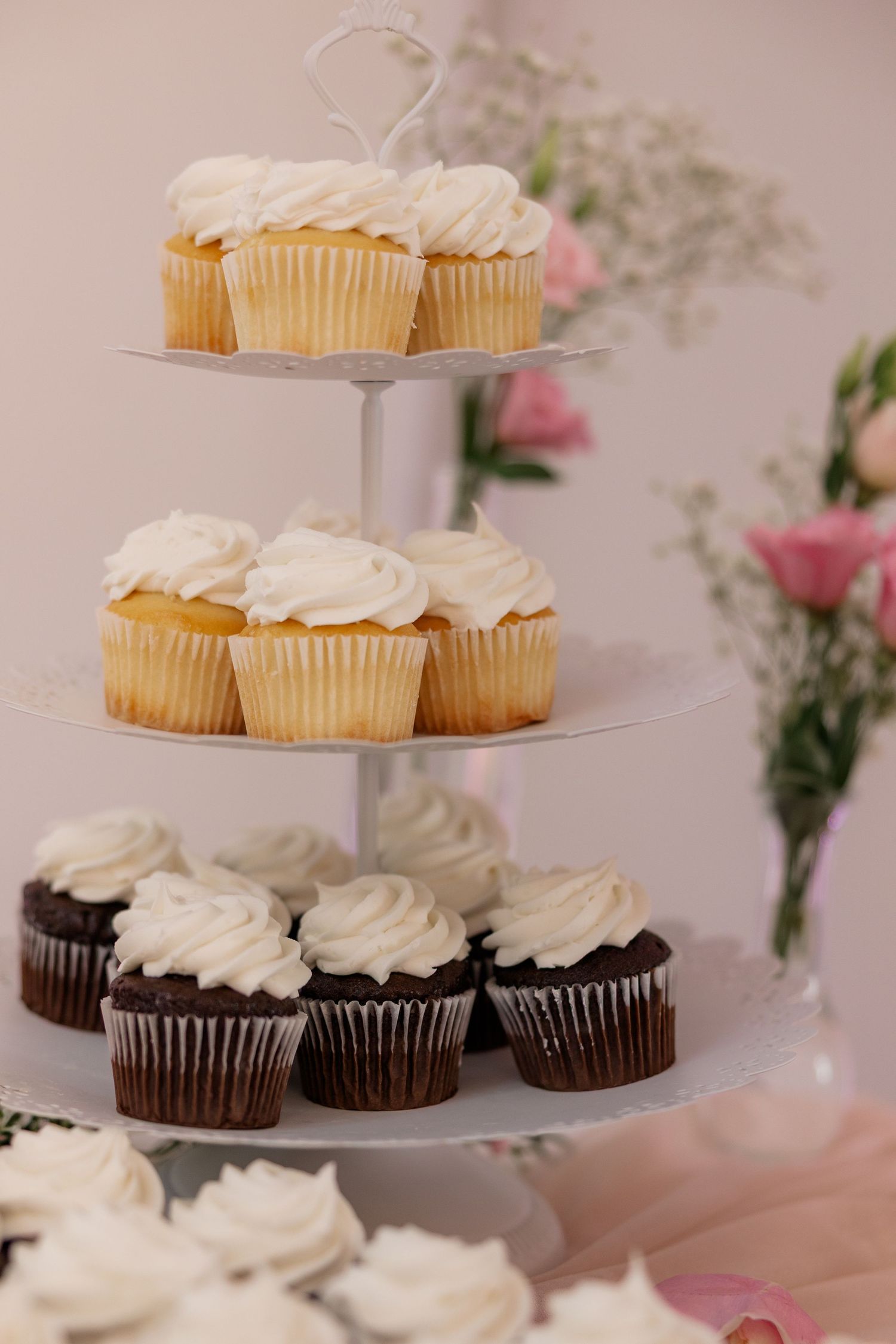 Tiered display of white-frosted cupcakes adorned with pink floral decorations.
