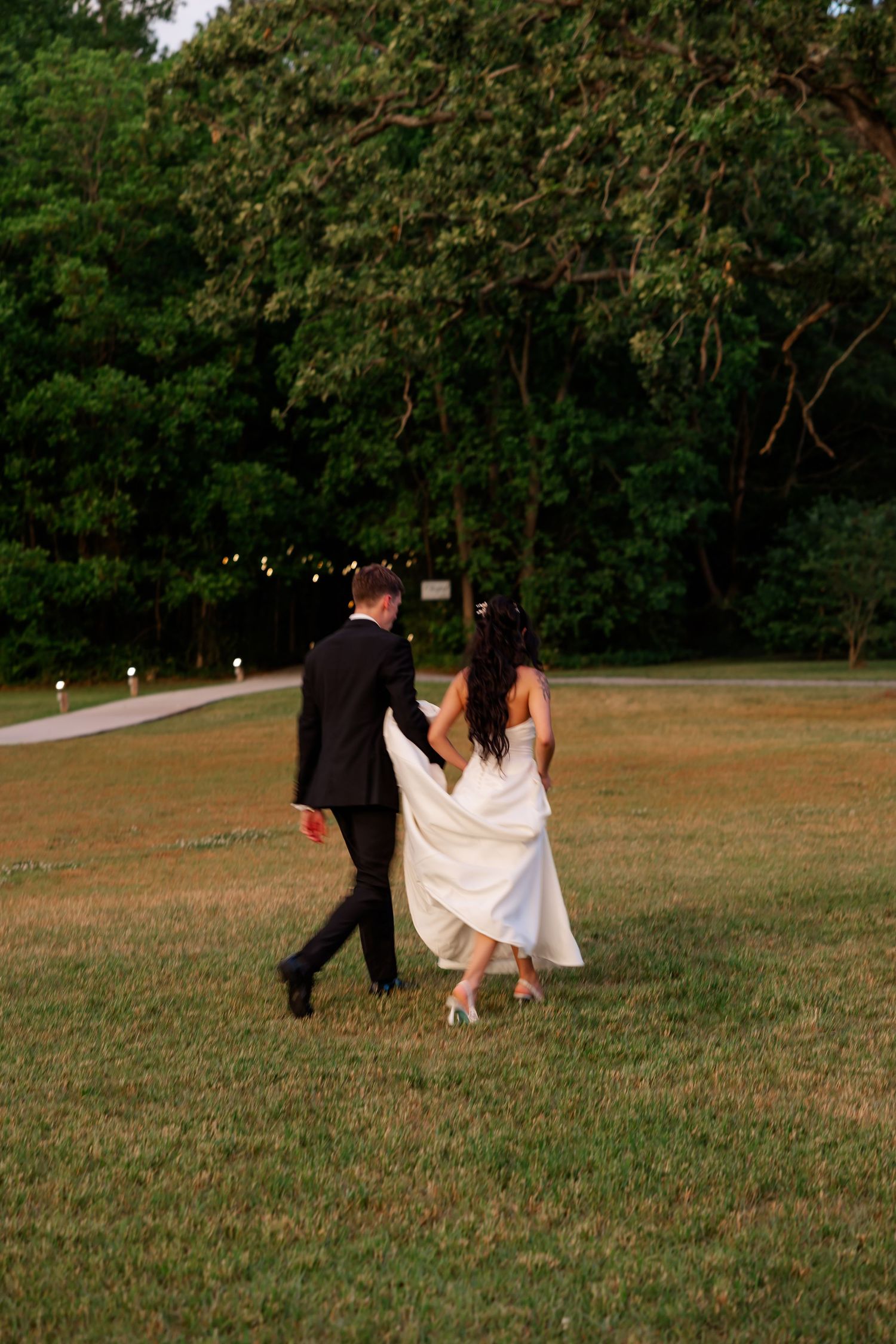 Couple walking together across a grassy field at their wedding.