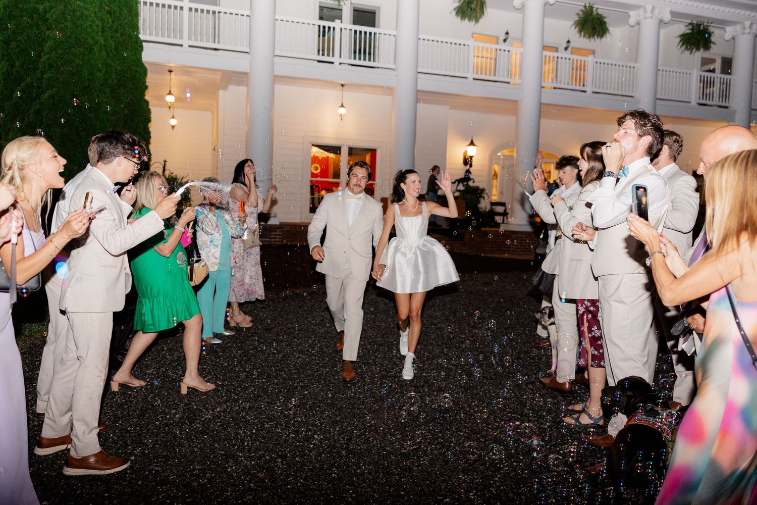 Large group of wedding guests dancing in formal attire at outdoor reception.