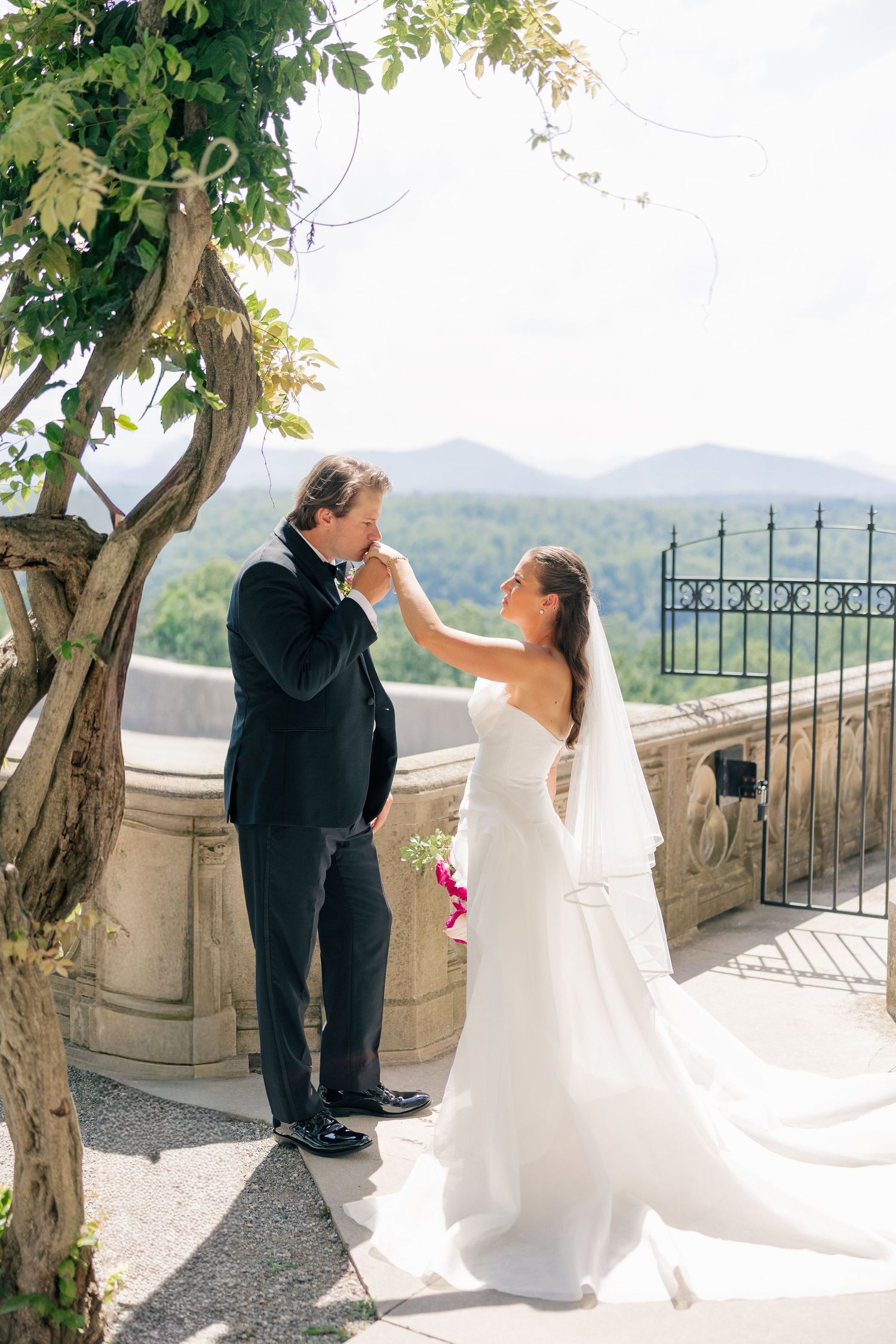 Bride and groom share a tender moment on a stone terrace with scenic mountain views.