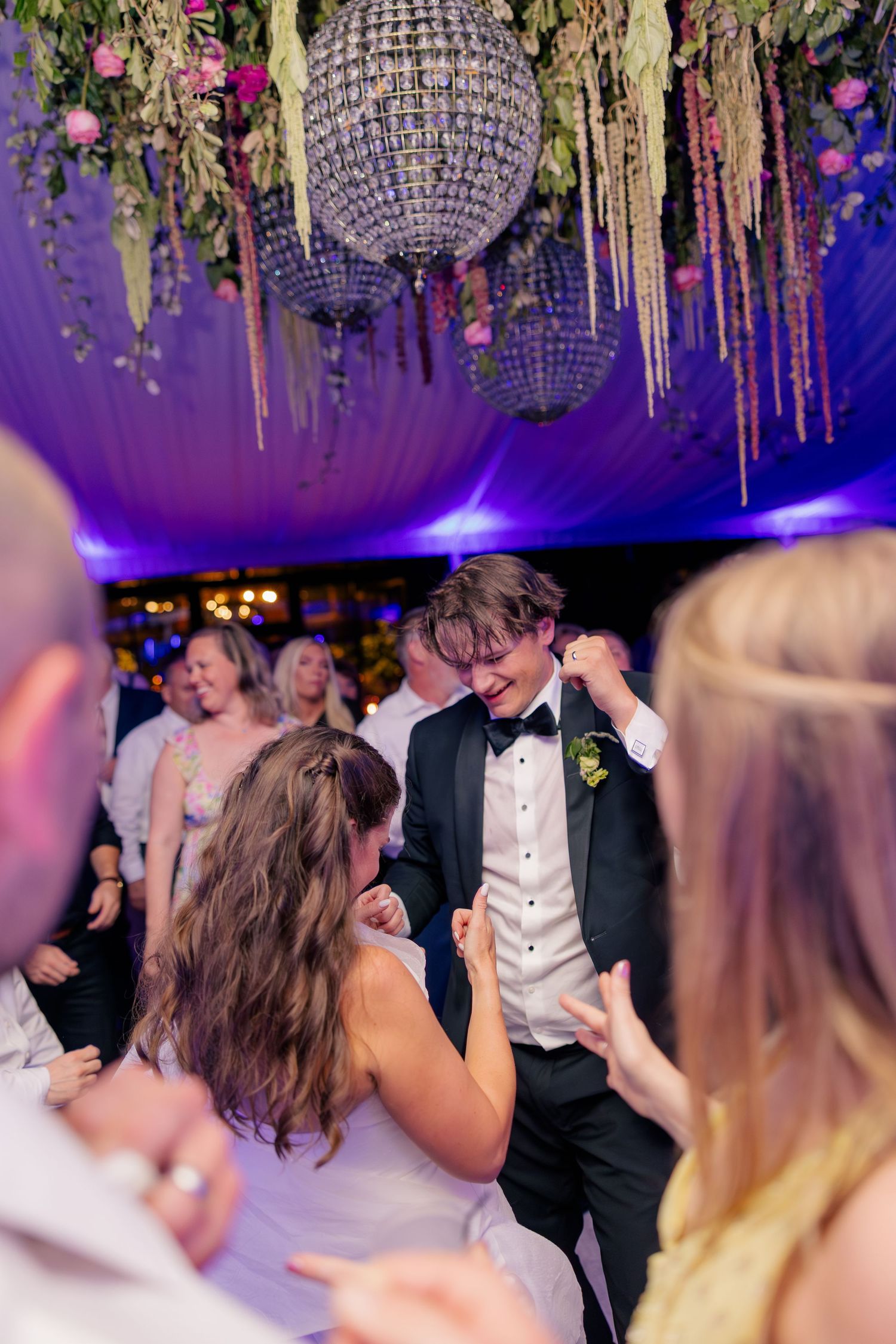 Bride and groom share a lively dance together under a crystal chandelier at their wedding reception.
