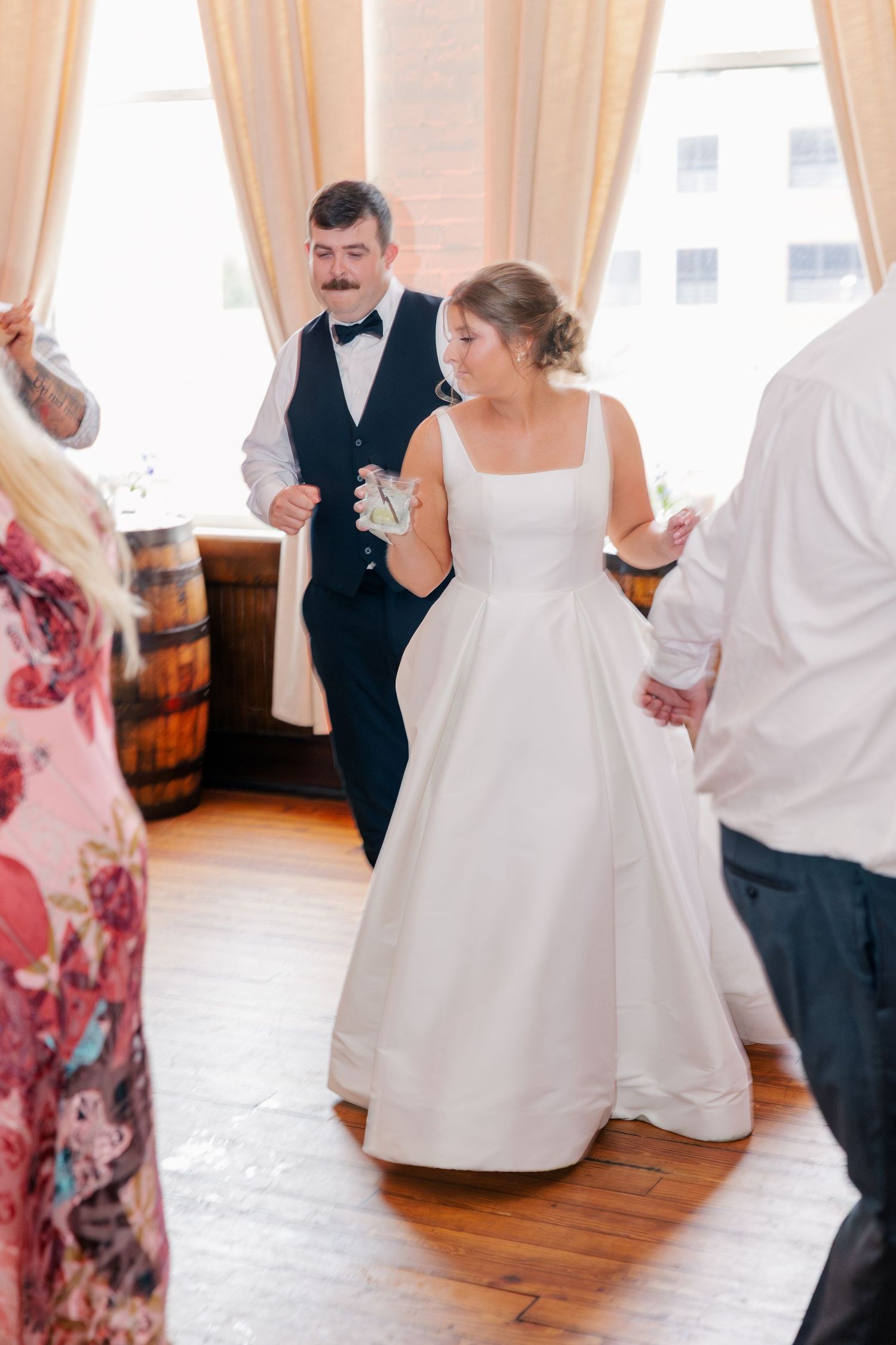 Bride in white gown and groom in navy suit dancing with guests at elegant wedding reception.