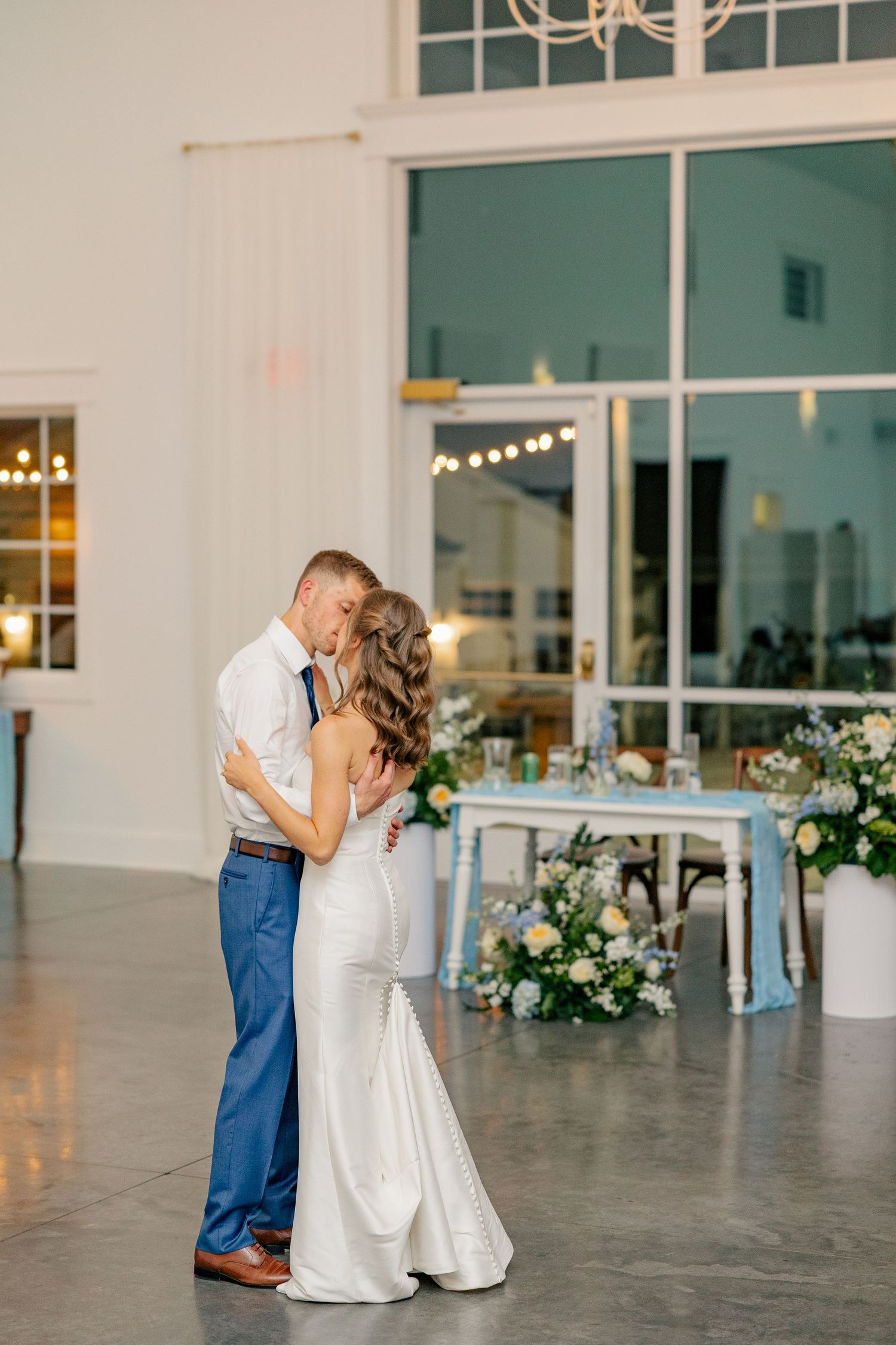 Couple shares romantic first dance kiss in bright modern wedding reception hall.