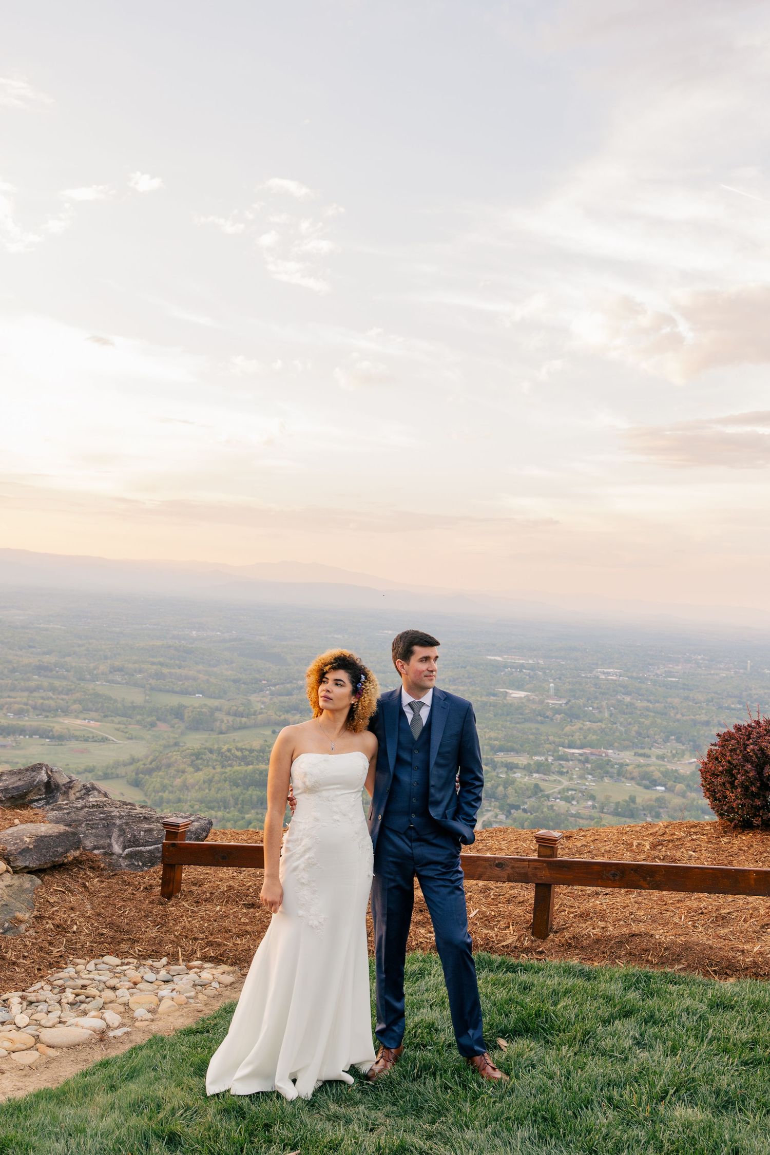 Bride and groom posing at sunset overlook with stunning panoramic valley views behind them.
