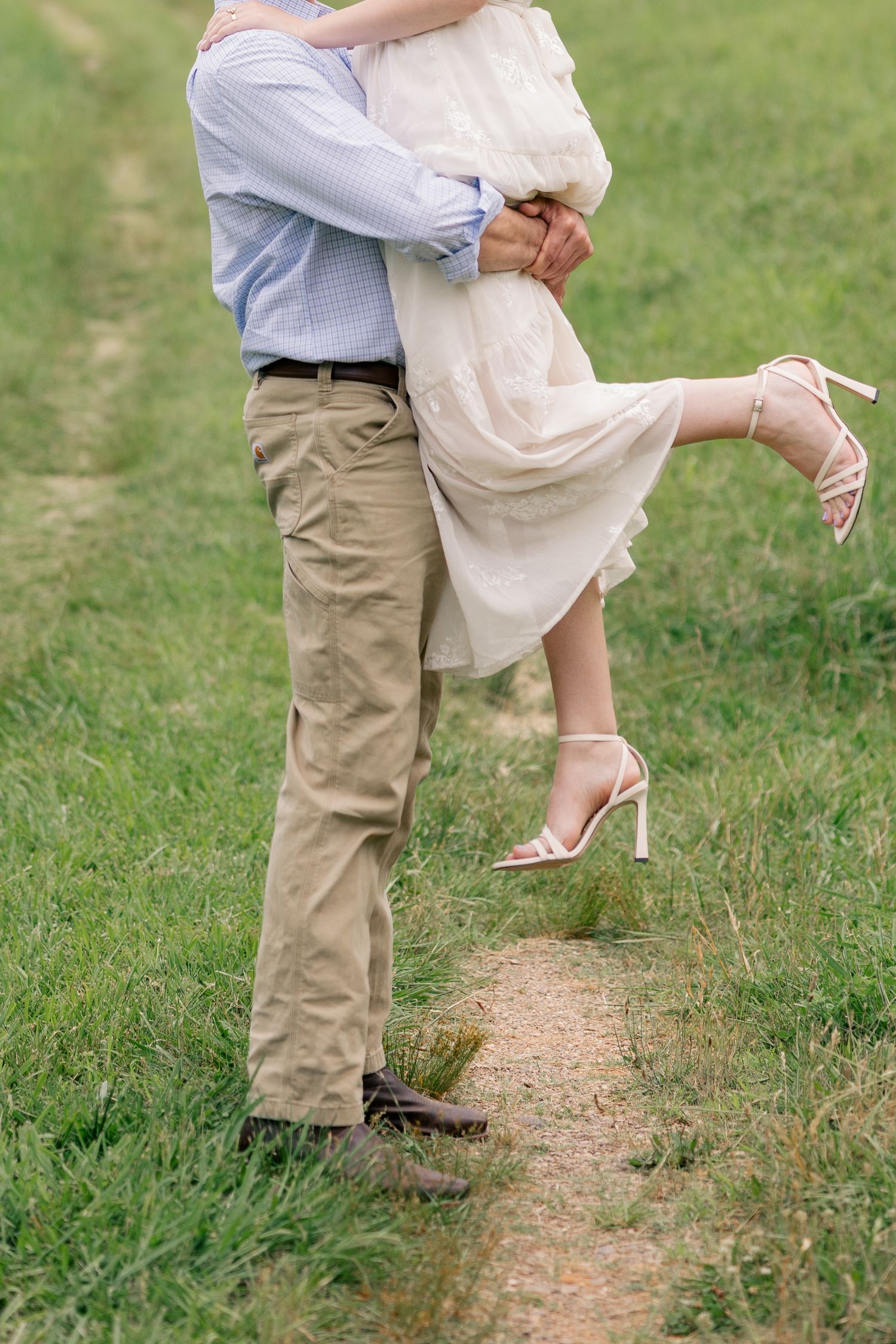A couple stands together outdoors showing their feet and lower legs in a romantic pose on grassy ground.
