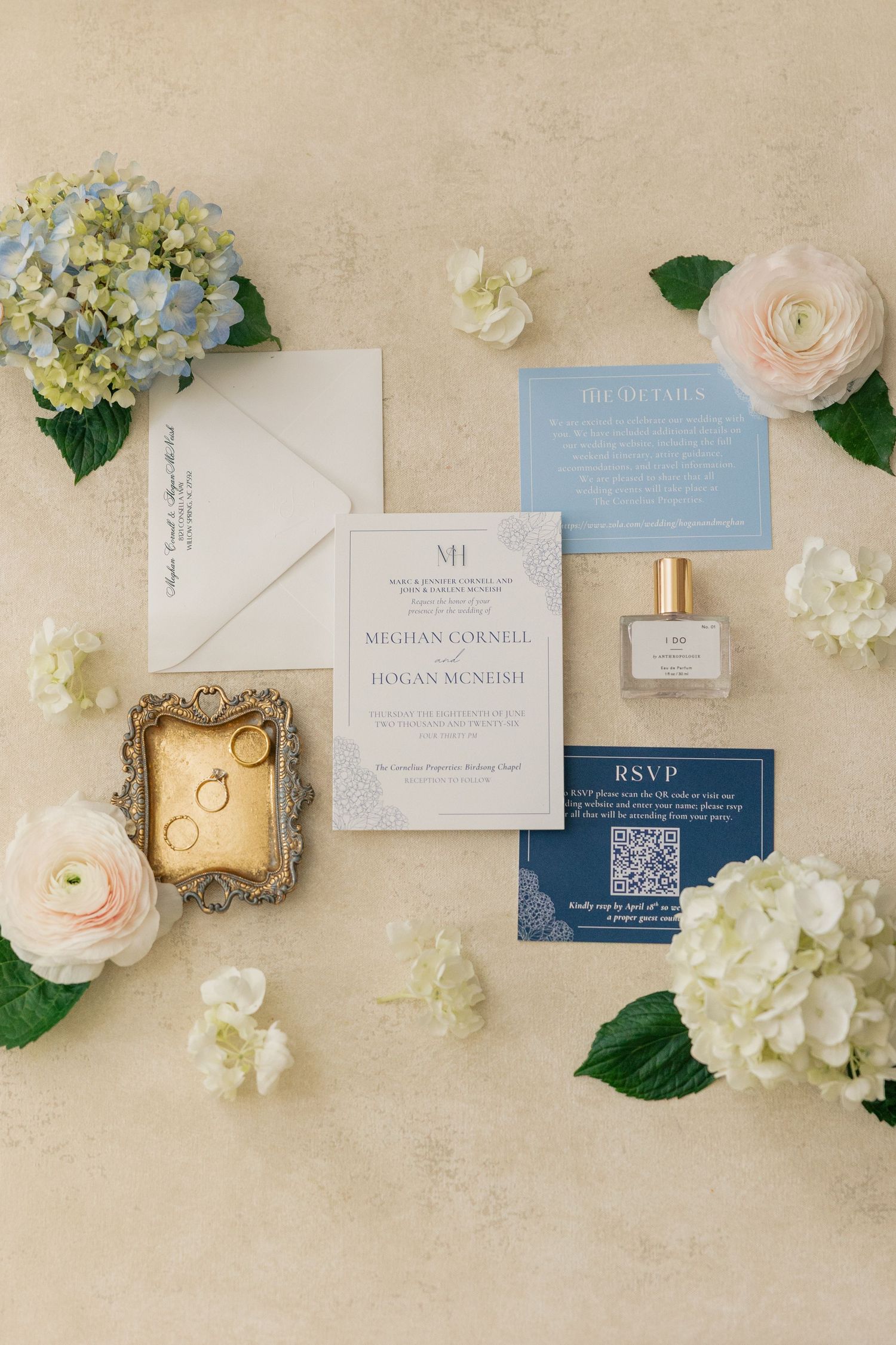 Elegant wedding stationery suite with blue hydrangeas, rings, and perfume on a neutral background.