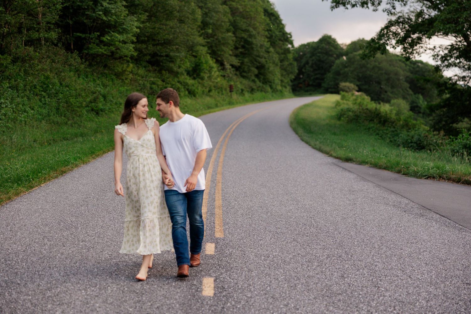 A couple walks together on a winding mountain road surrounded by lush greenery.
