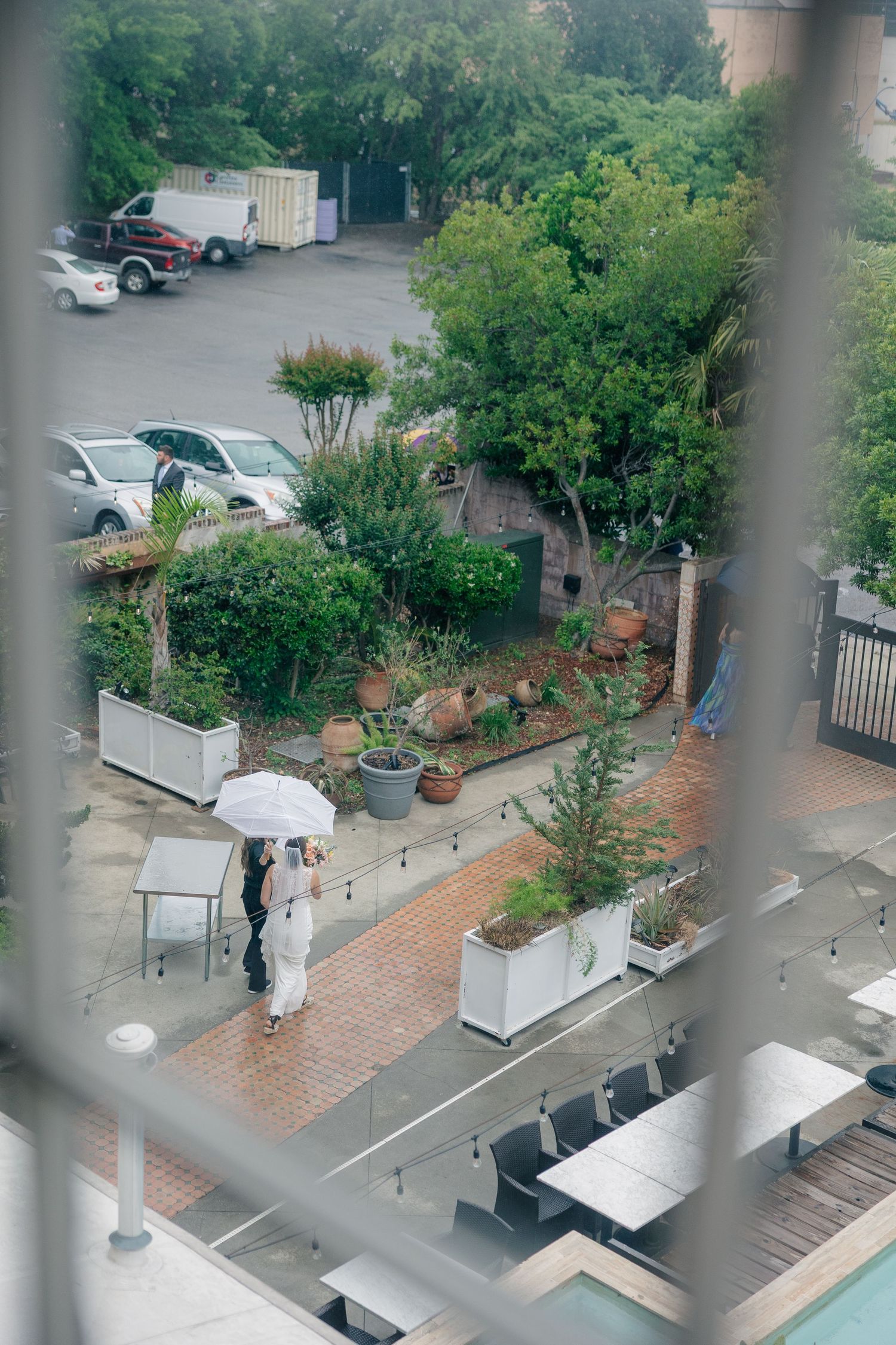 Bride and groom share intimate moment under white umbrella on rainy wedding day, viewed from above.