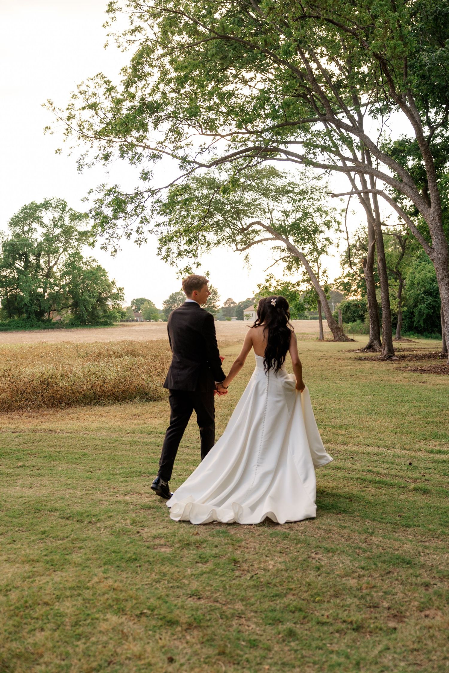 Wedding couple walking together through a scenic field at sunset.