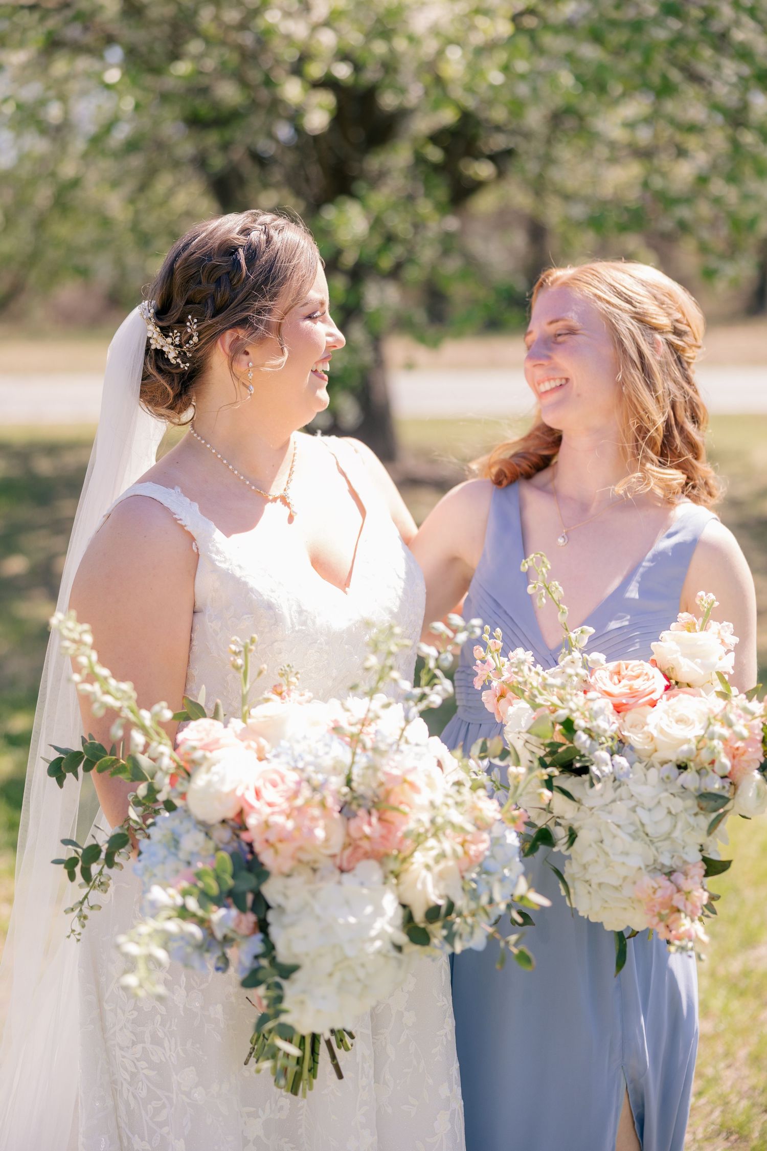 Wedding party members in blue and white dresses hold beautiful peach and white floral bouquets.