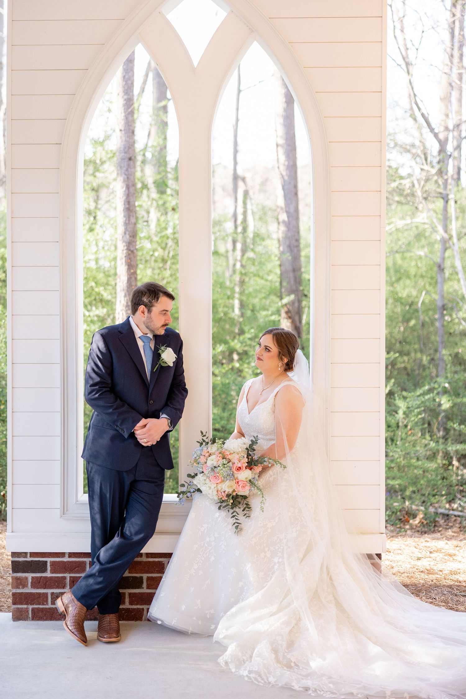 Newlyweds share an intimate moment under a white columned porch during their wedding day.