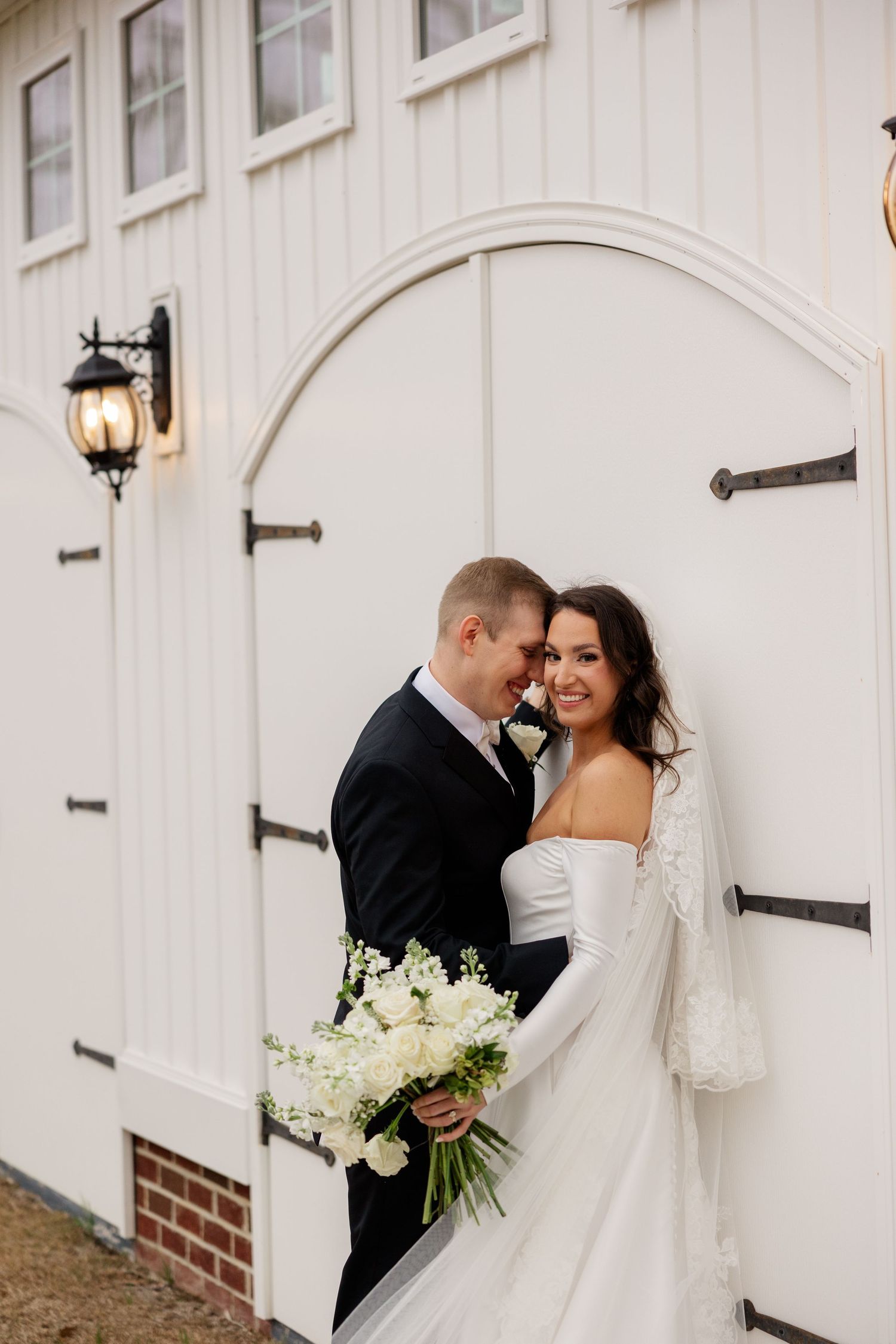 Romantic wedding portrait against white barn door with bouquet.