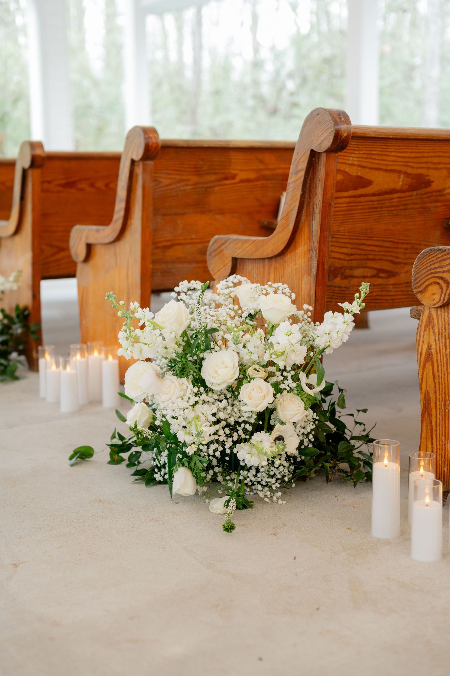 White floral arrangements with candles decorate wooden church pews for a wedding ceremony.