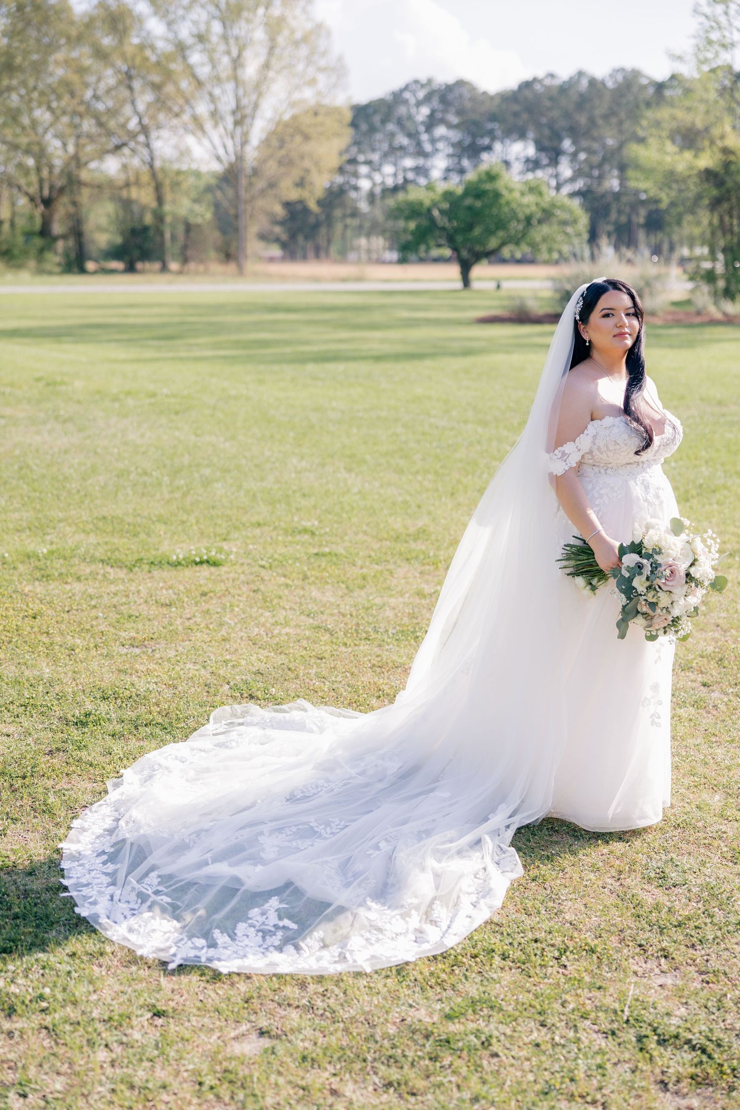 Wedding gown with elegant train flows across grassy field during bridal portraits.
