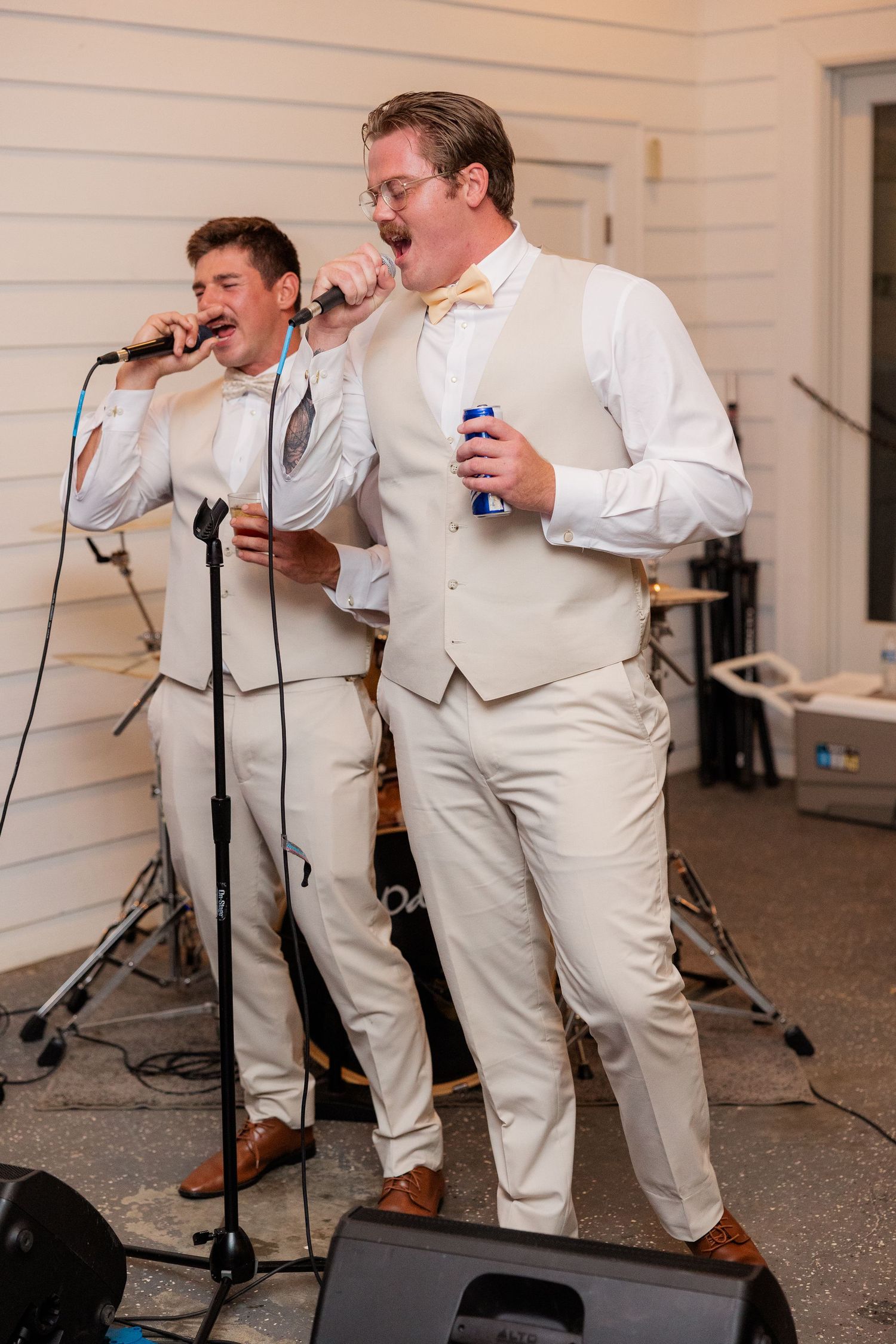 Groomsmen in white suits perform and sing with microphones during wedding reception entertainment.