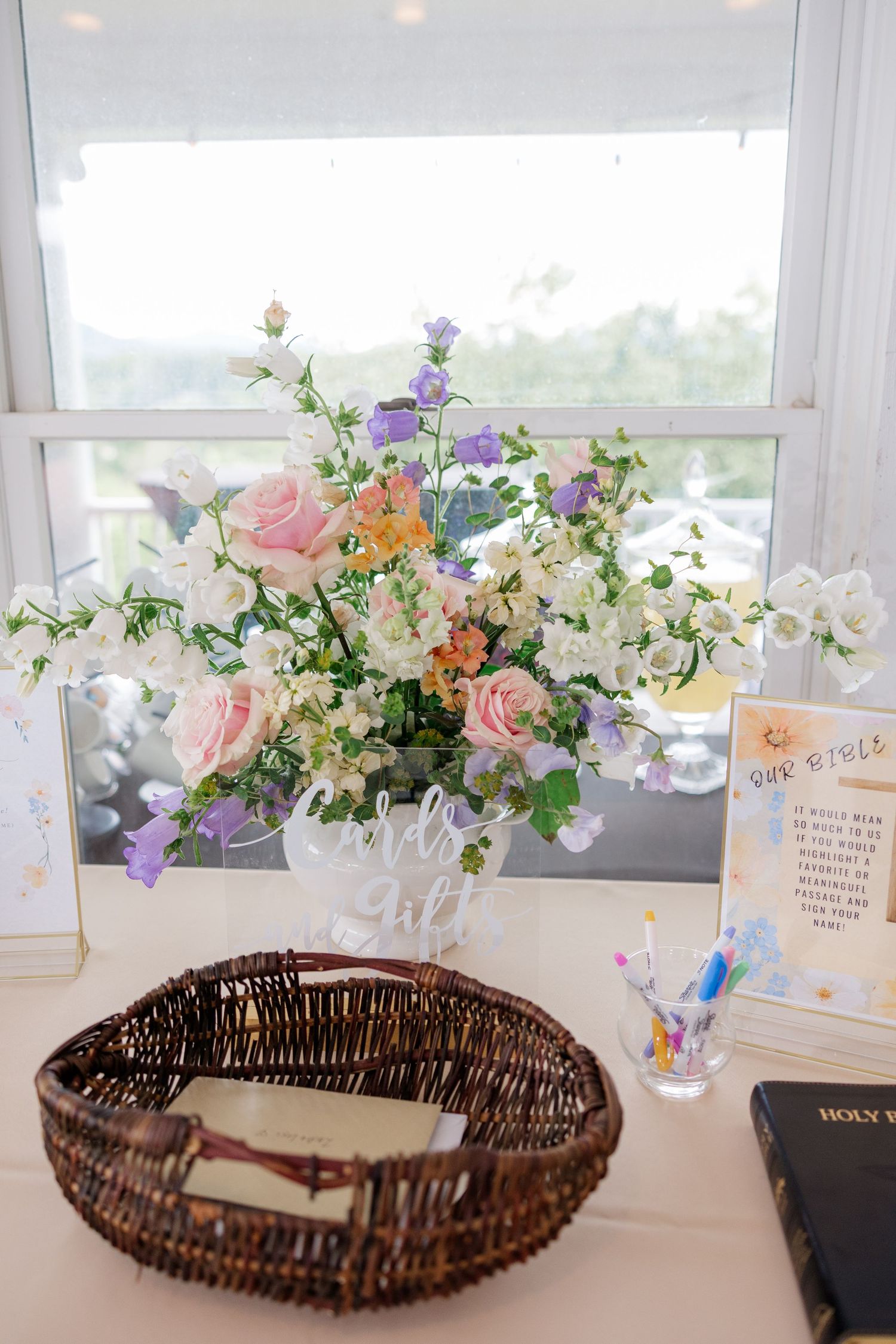 Delicate floral centerpieces with pink roses and white flowers alongside wicker baskets on a reception table.