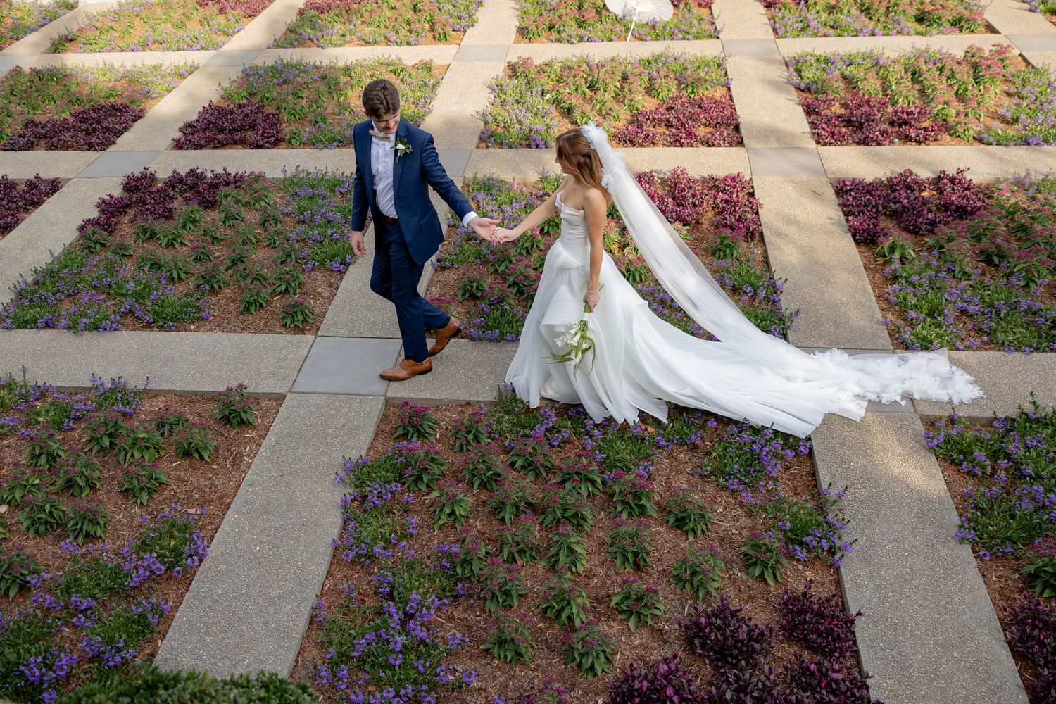 Wedding couple walking through geometric garden paths with colorful flower beds.