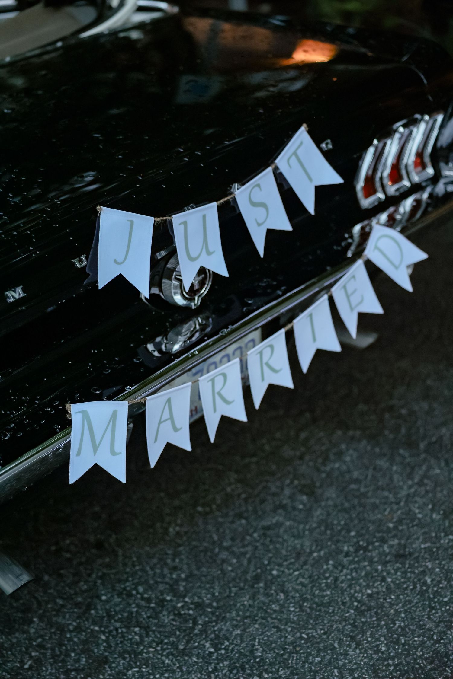 Black classic car decorated with Just Married pennant banner sign at wedding reception celebration.