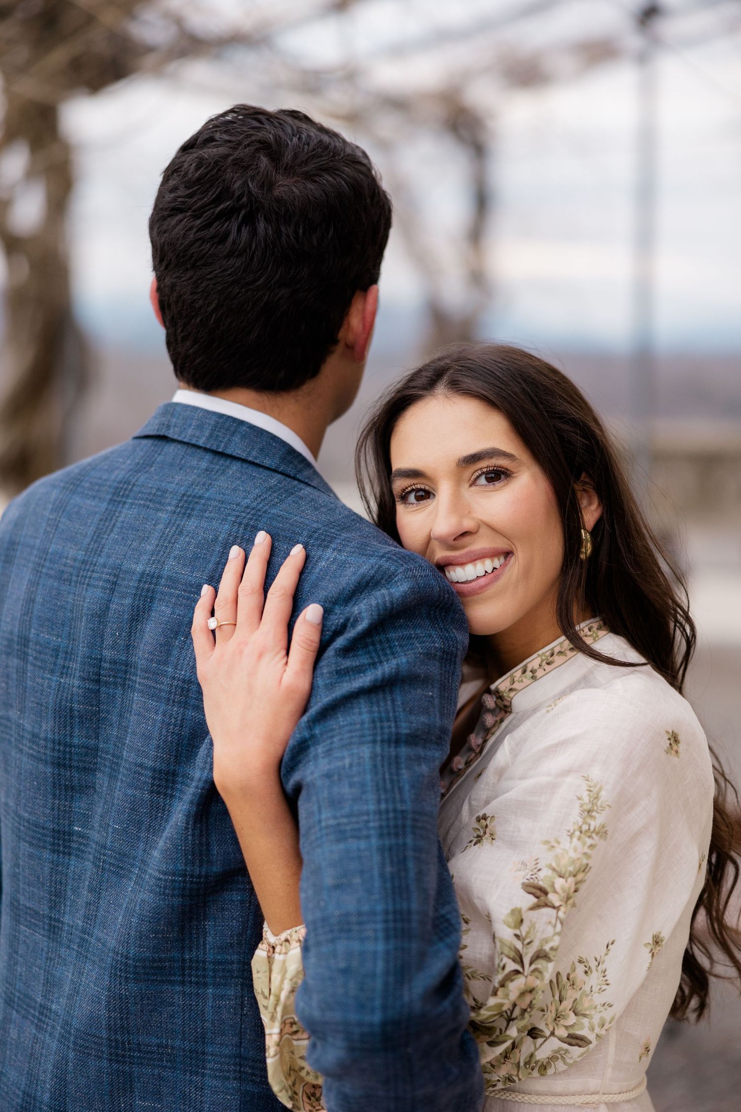 A newly engaged couple in formal attire embraces during an outdoor photo session.