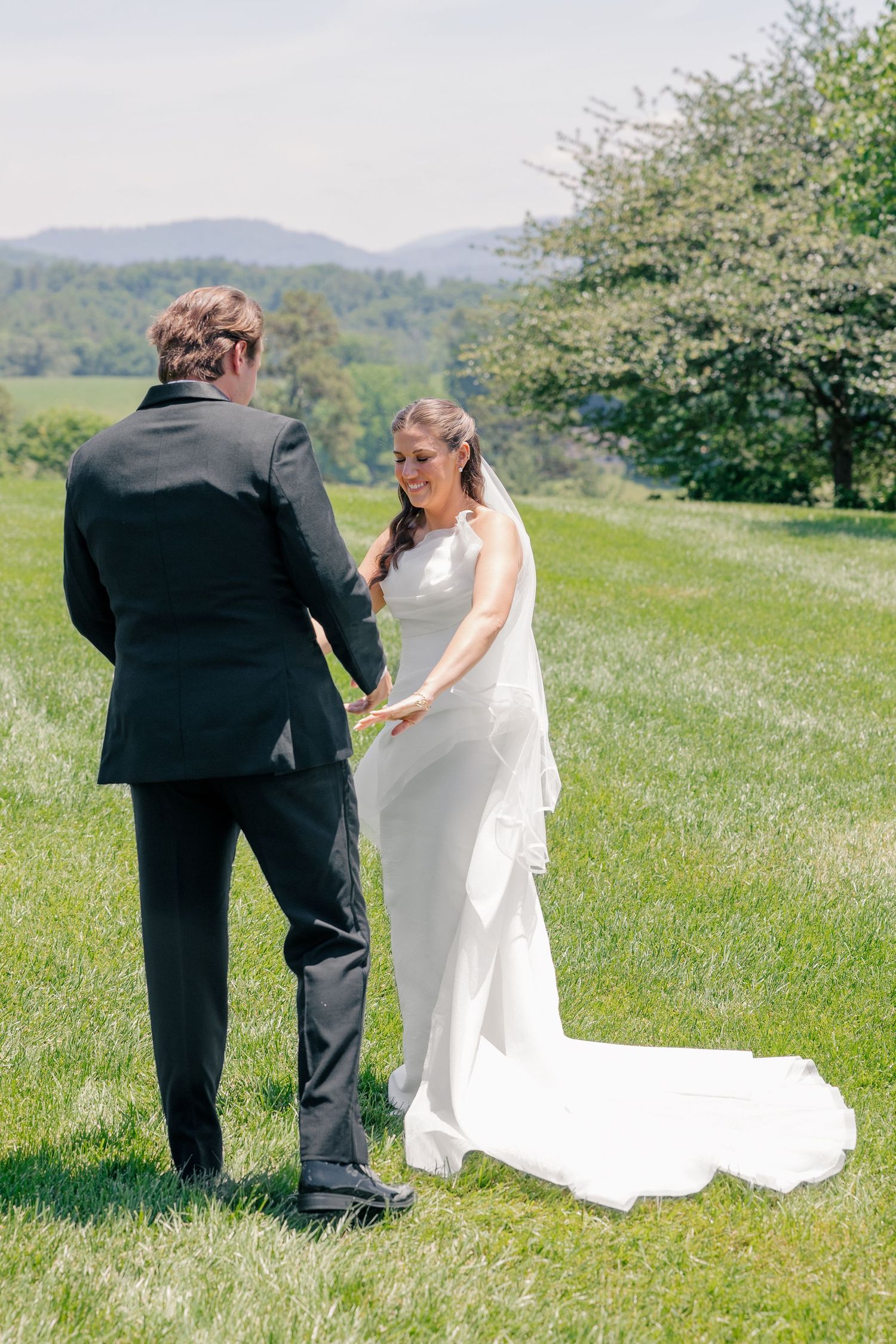 Bride and groom share a first look moment on a lush green lawn with mountain views in the background.