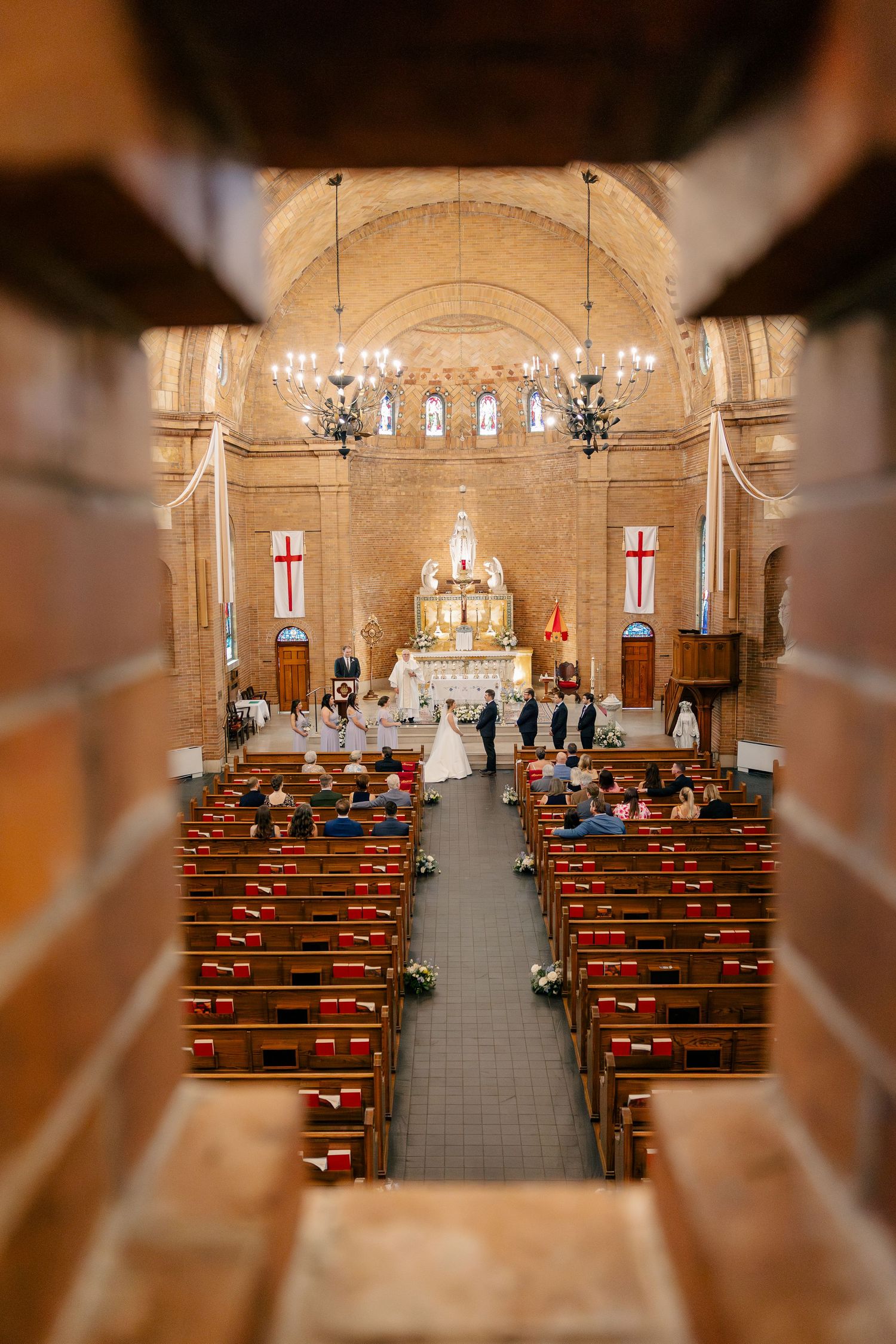 Wide-angle view of an intimate Catholic church wedding ceremony through wooden balcony railings.