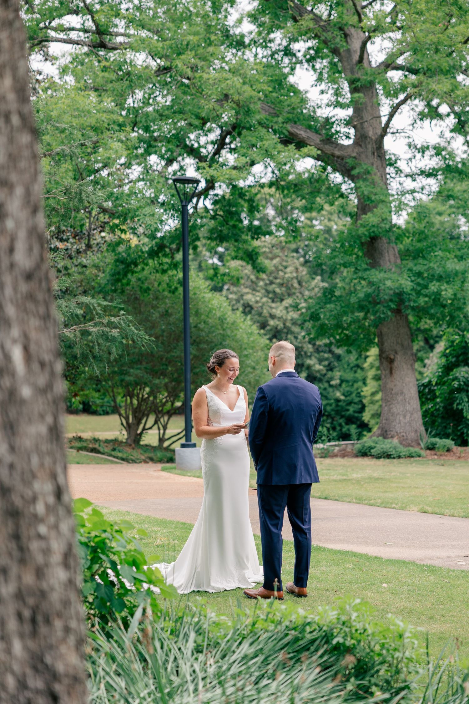 Bride reads vows to groom during intimate outdoor first look ceremony in lush green park setting.