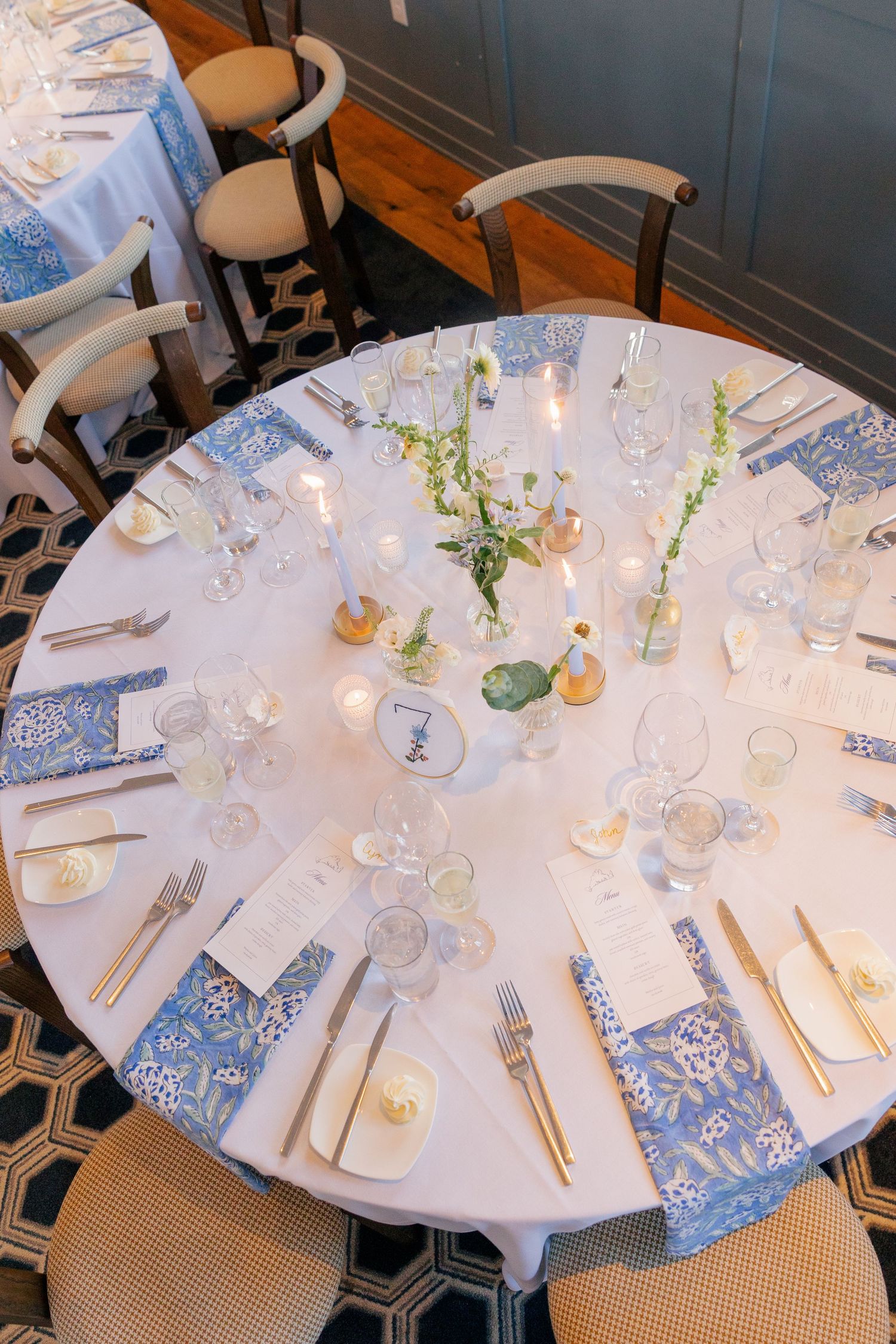 Elegant wedding reception table set with blue patterned napkins, candles, and floral centerpieces.