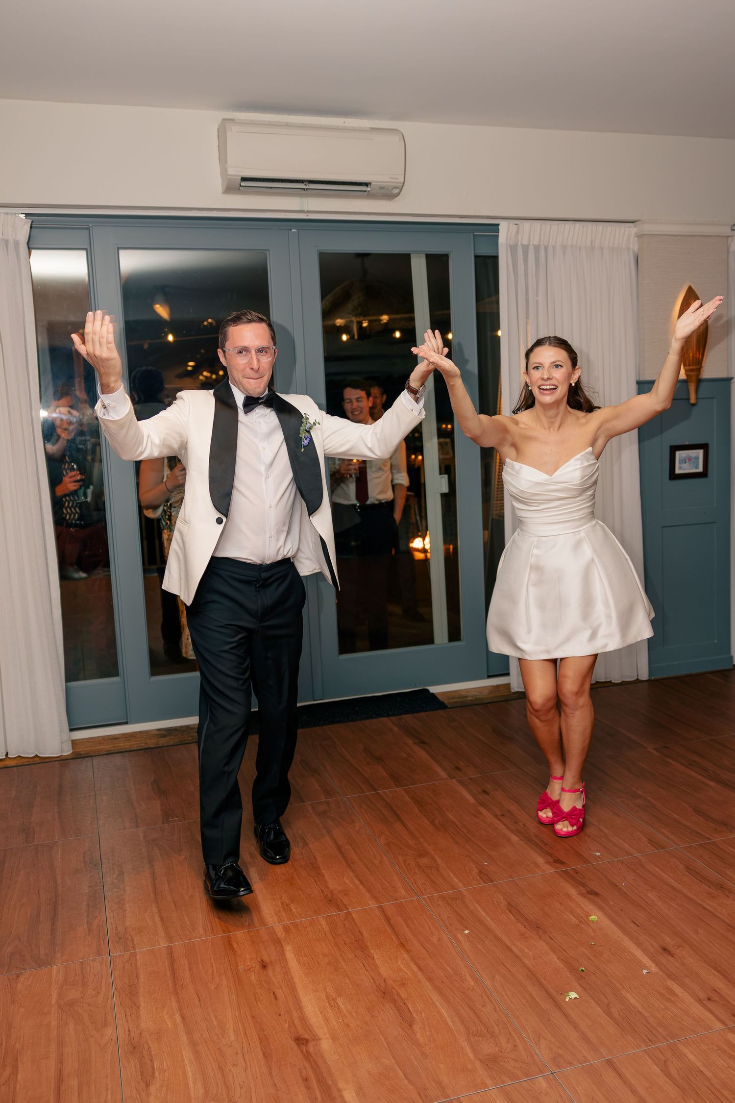 Newlywed couple makes grand entrance onto dance floor with arms raised in celebration at wedding reception.