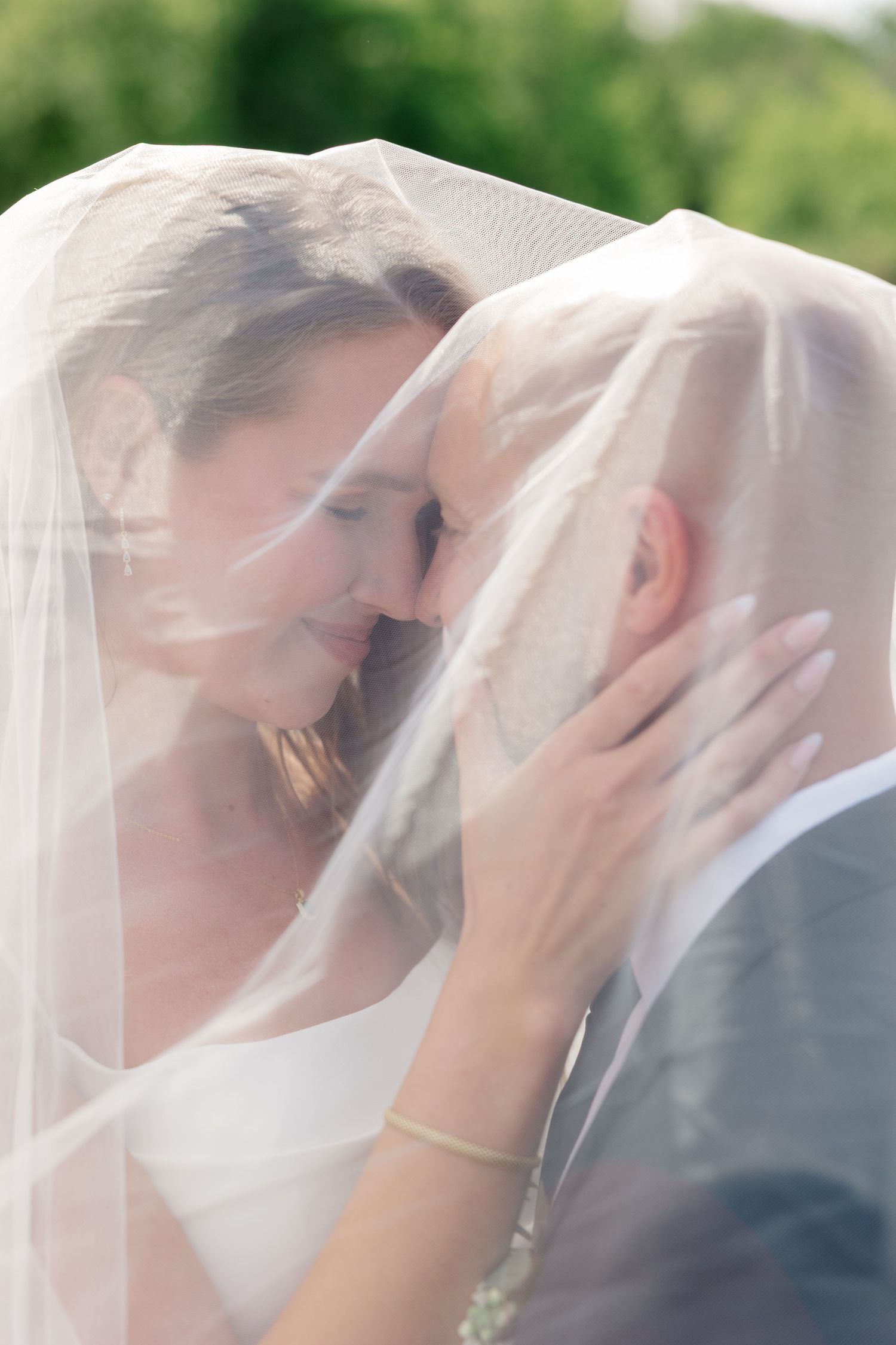 Tender moment between newlyweds sharing a kiss under a delicate white veil.