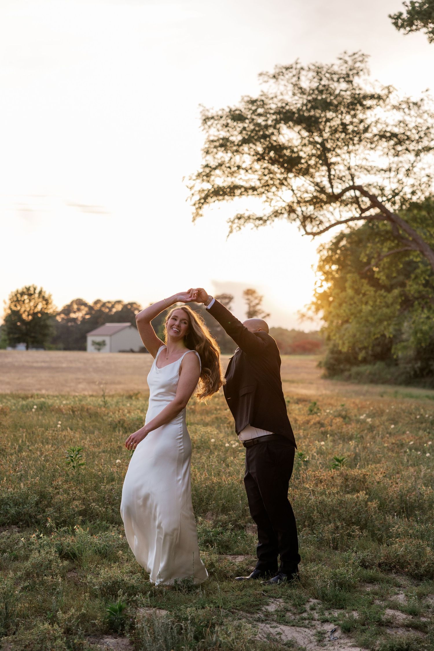 A couple dancing in a field at sunset with the bride's dress flowing in golden light.