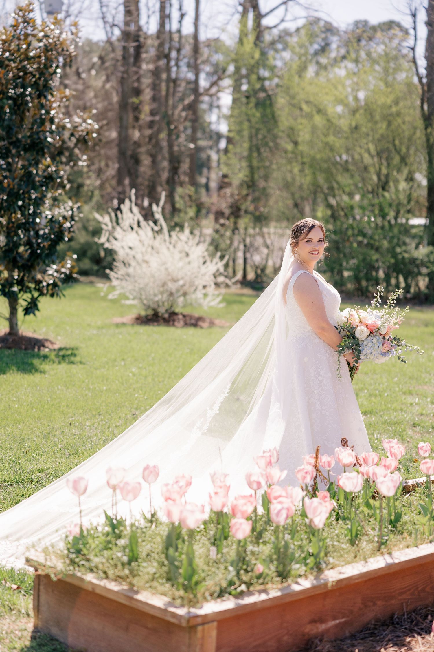 A flowing white wedding gown train spreads across a flower garden in springtime.