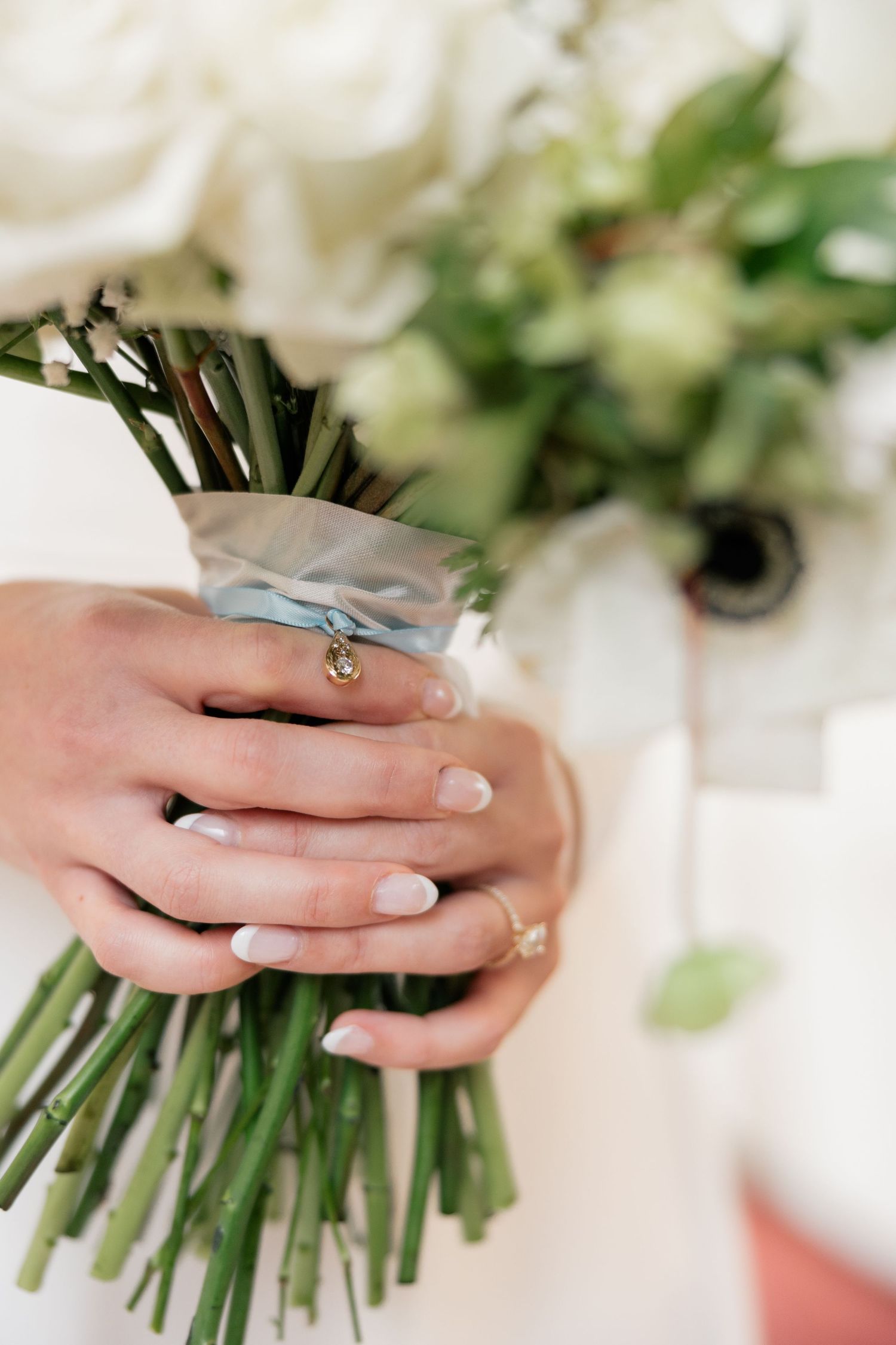 Hands delicately holding a classic white wedding bouquet tied with ribbon.