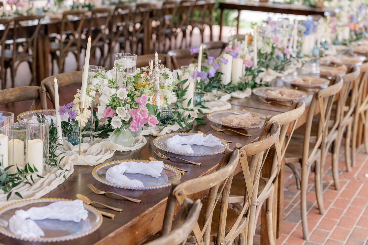 Elegant wedding table setting with pink floral arrangements and cross-back chairs at an outdoor reception.