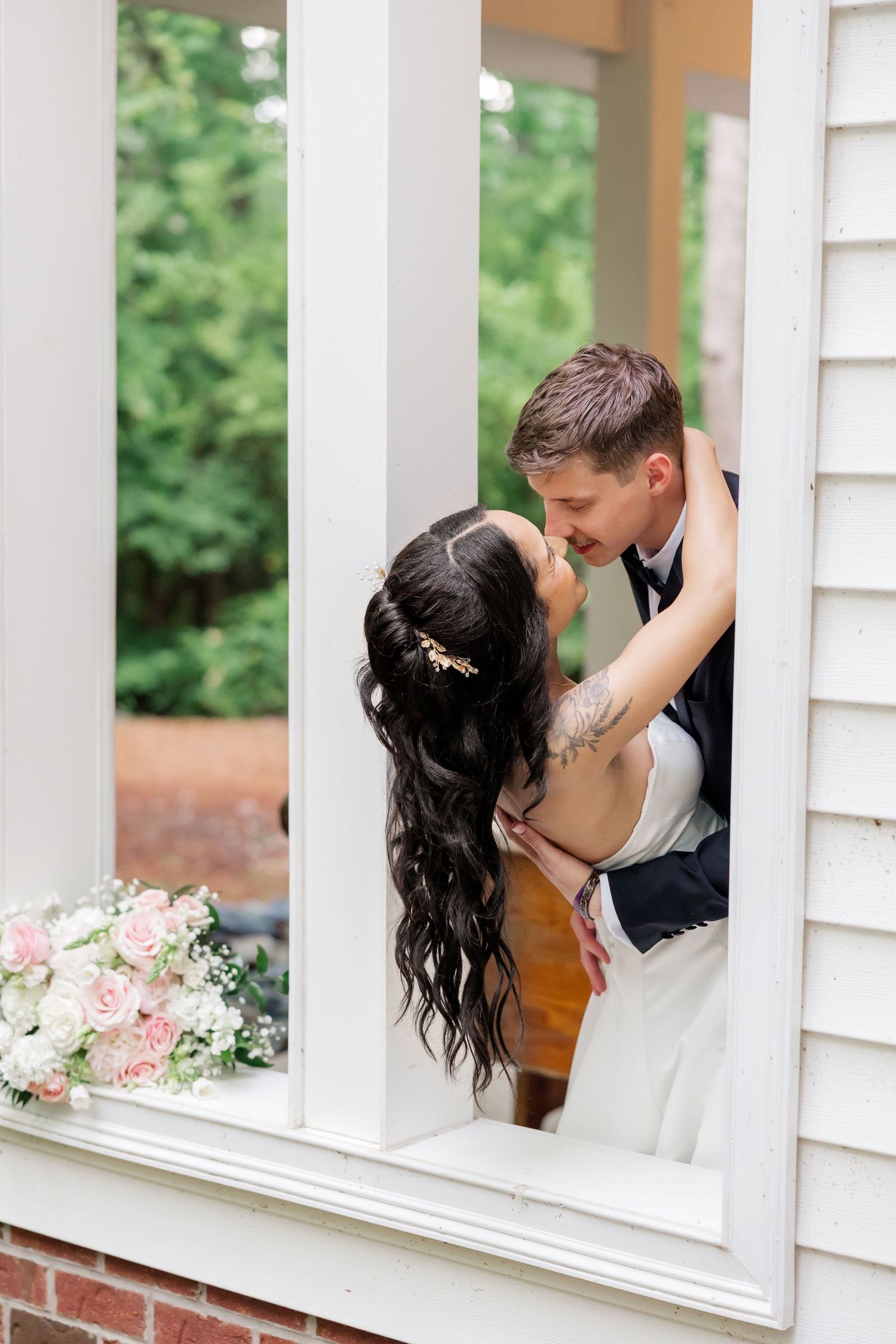 Romantic couple shares intimate moments through a white porch railing with pink floral decorations.