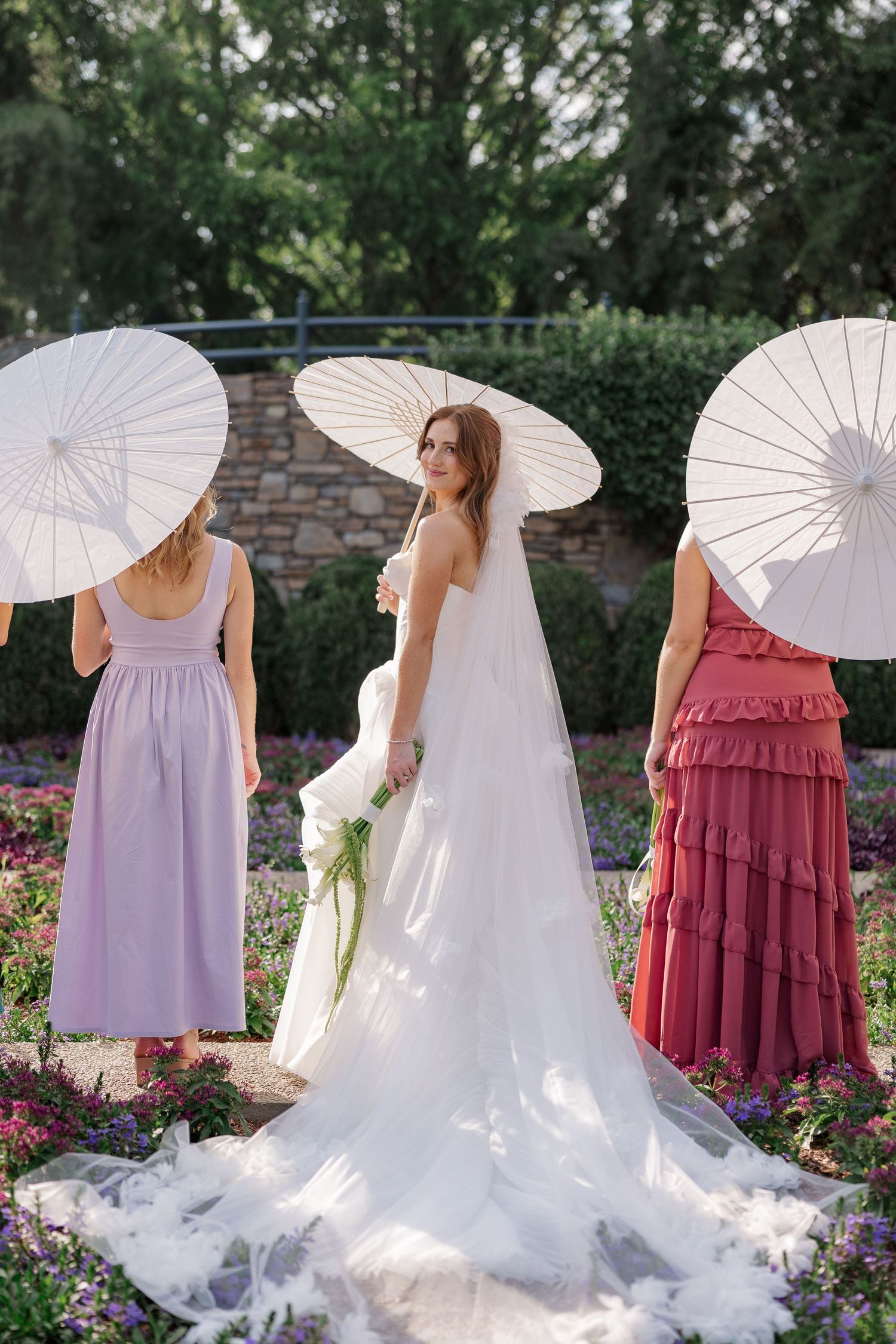 Three attendees with white parasols pose in a garden setting.